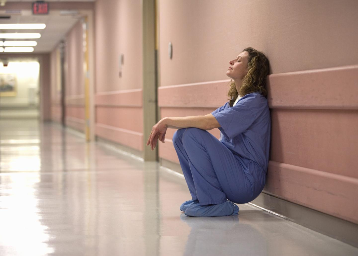 Female doctor leaning against wall in hospital corridor, side view