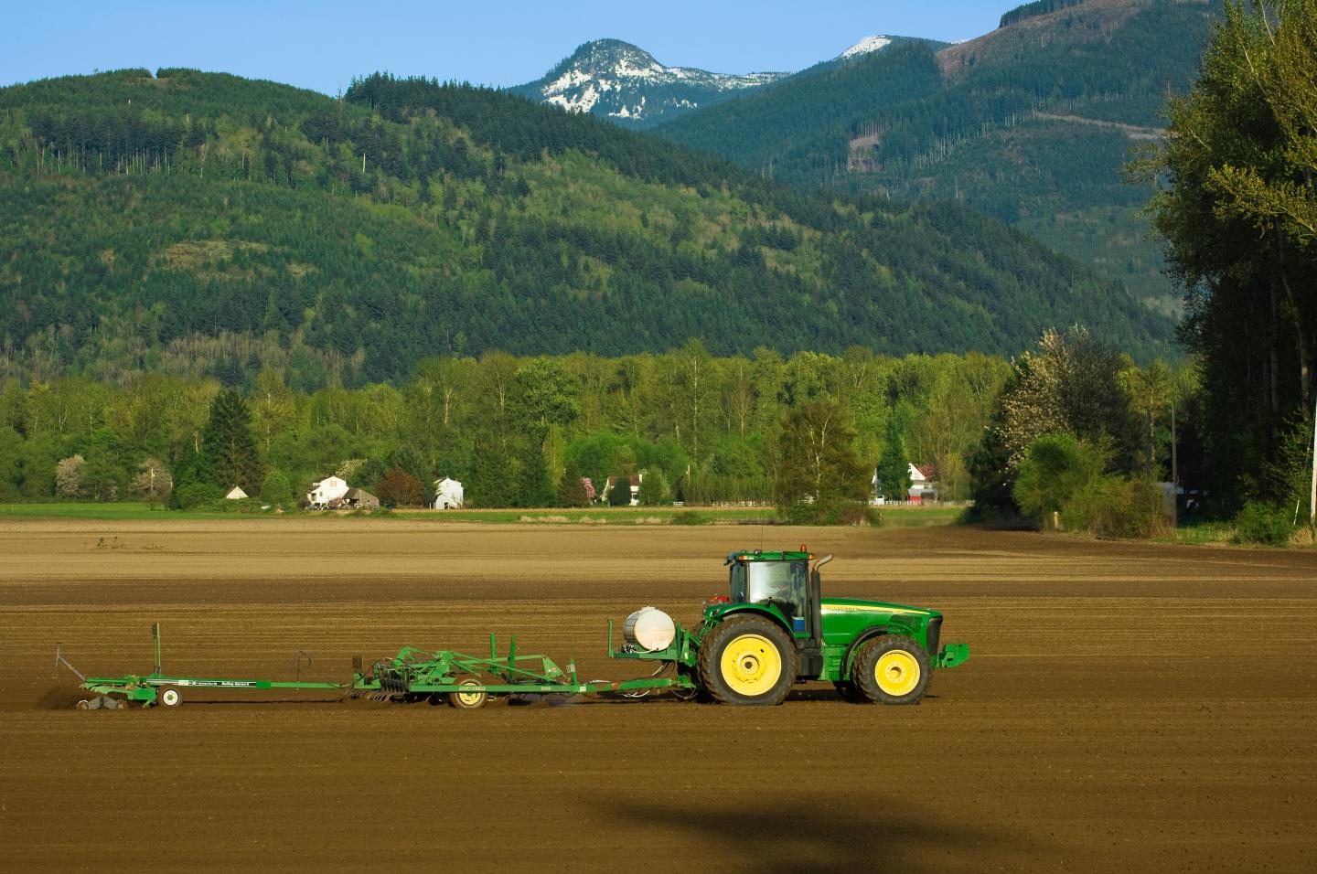A John Deere tractor pulling a chisel plow and rotary harrow to prepare a seedbed for planting potatoes near Burlington, Wash.