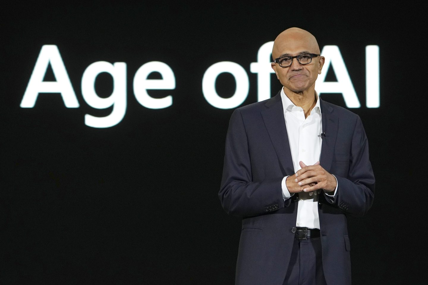 Microsoft CEO Satya Nadella frowning while standing in front of a sign that says "Age of AI"