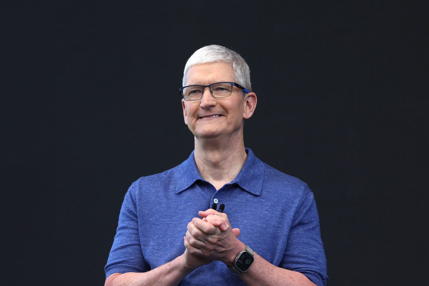Apple CEO Tim Cook clasps his hands together looking pleased