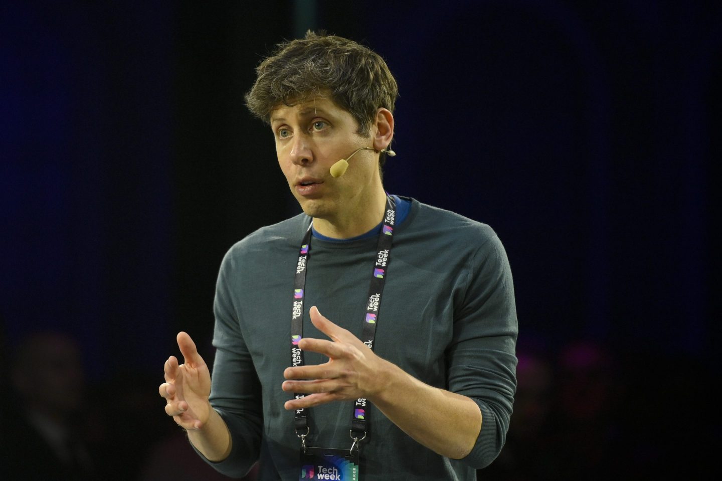 Sam Altman holds his hands up while speaking to an audience