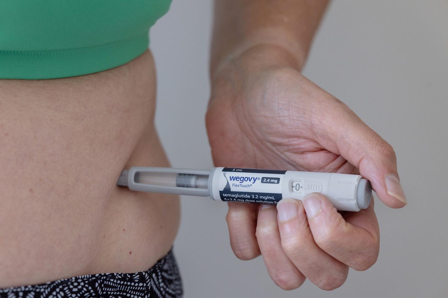 A person, with only the midsection visible, injects Wegovy under the skin of their stomach.