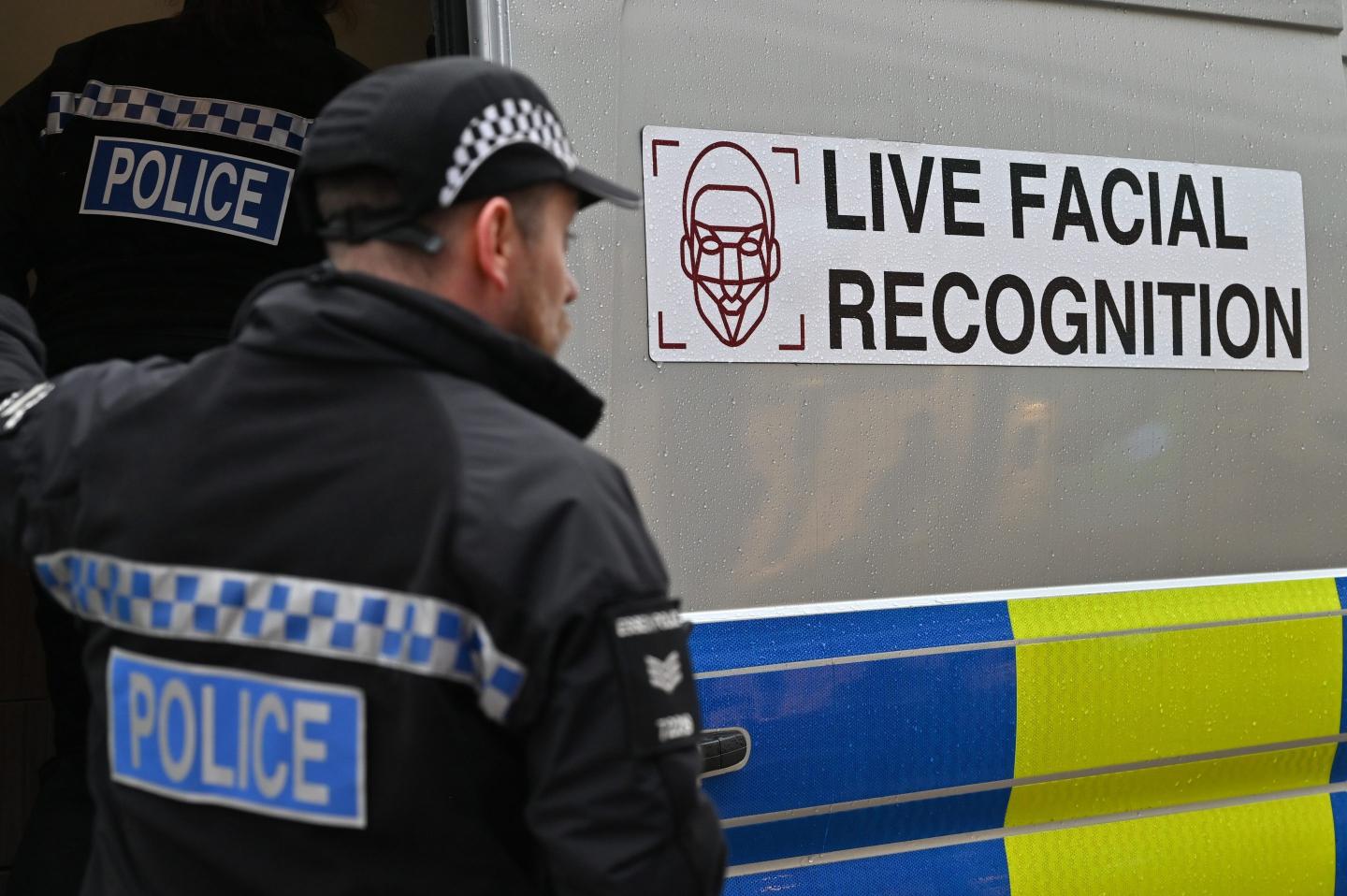 A British police officer stands in front of a police van with a sign warning the public that the police are using live facial recognition technology.