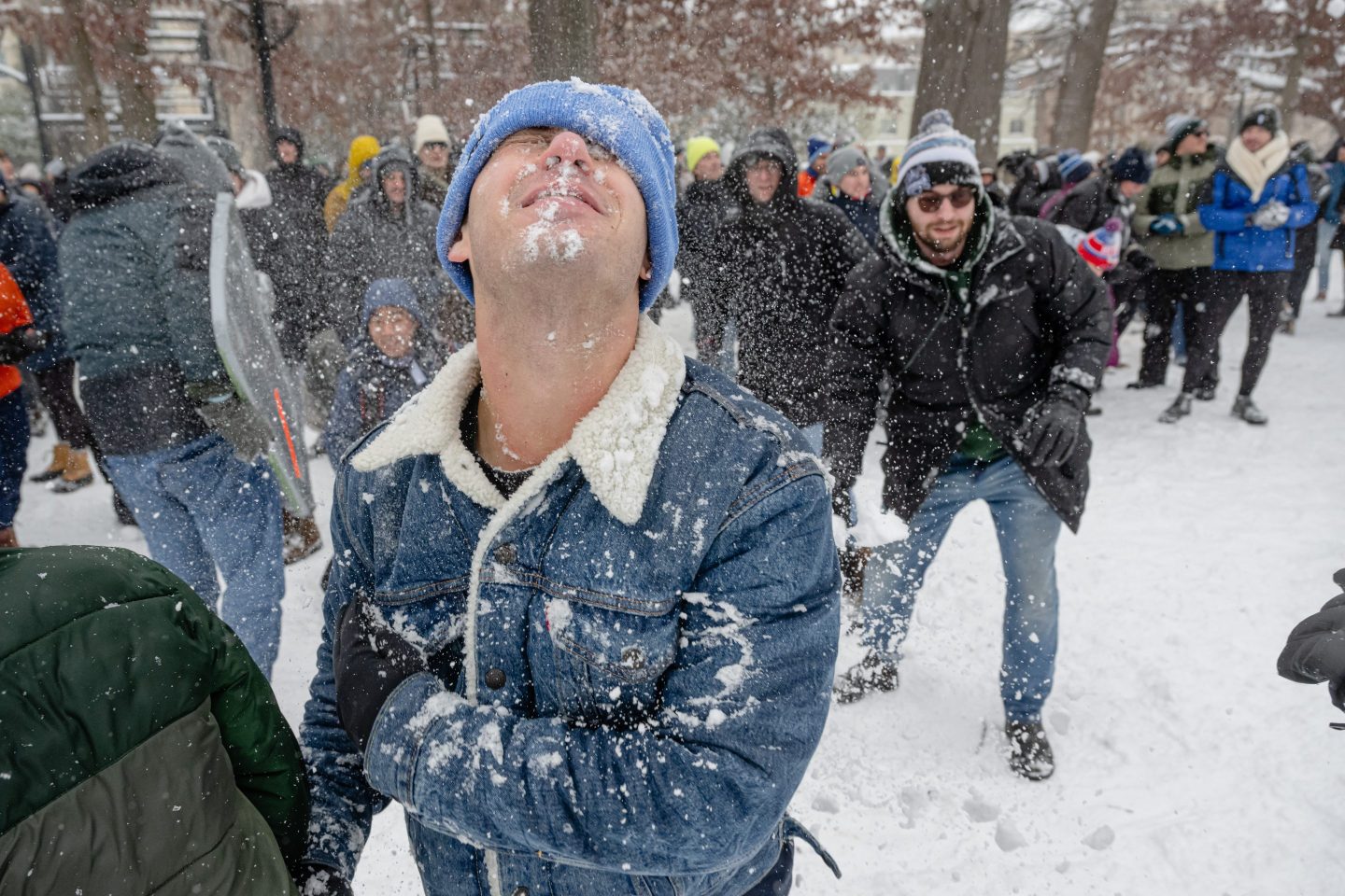 A person in a blue hat and denim jacket participates in a snowball fight