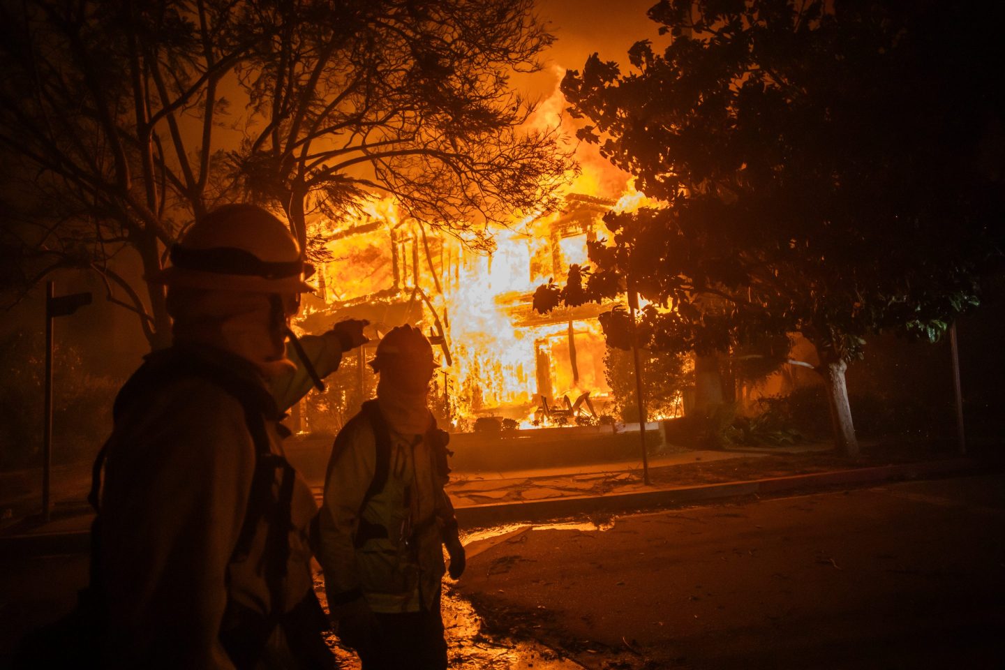 A Firefighter walks by a home on flames from the Palisades Fire during a powerful windstorm on January 8, 2025