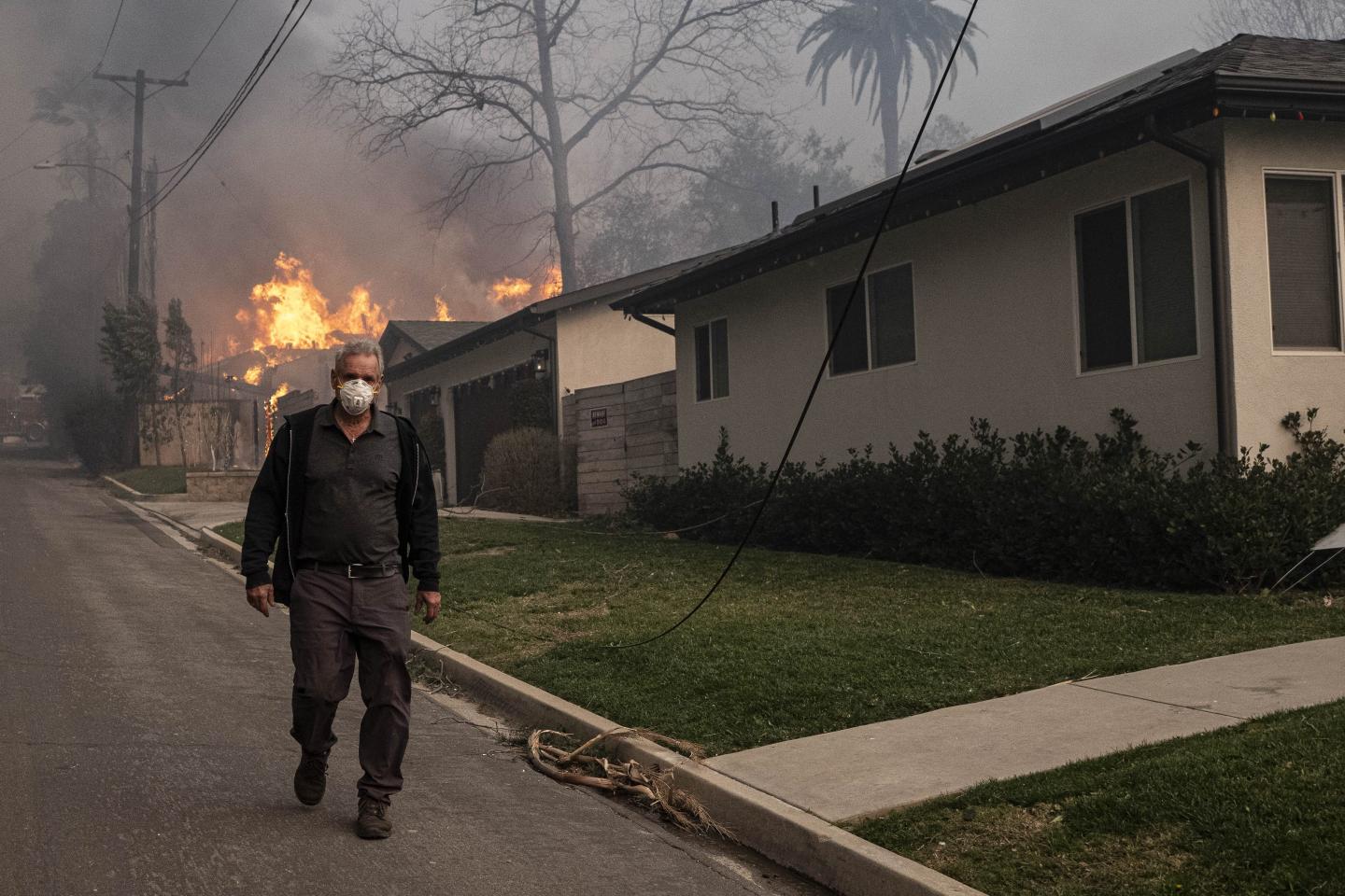 Man in a face mask walks away from his burning house