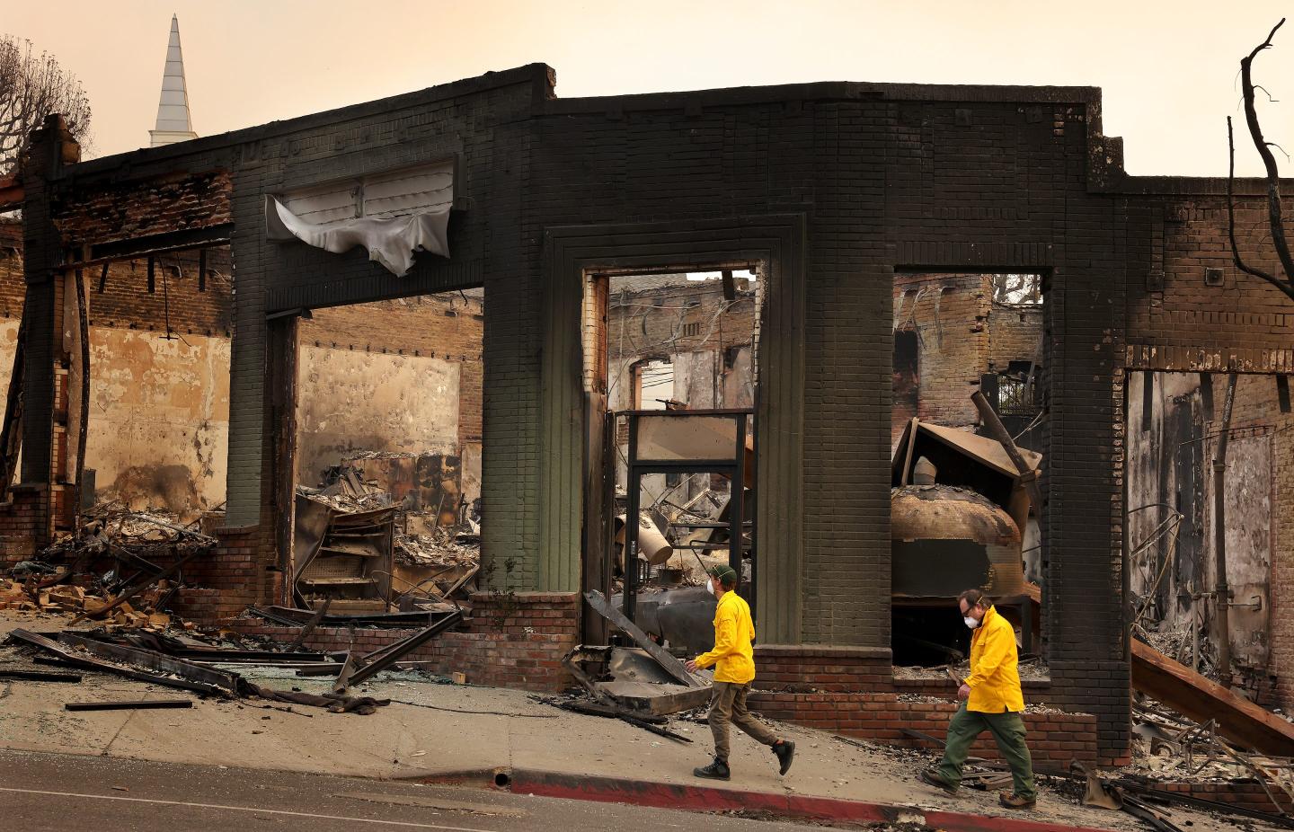 People walking in front of wildfire-damaged buildings.