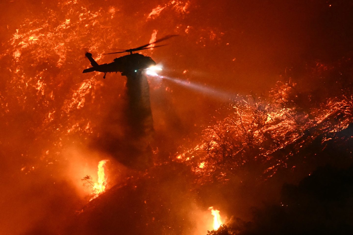 A helicopter flies over a fiery hillside during Los Angeles wildfires
