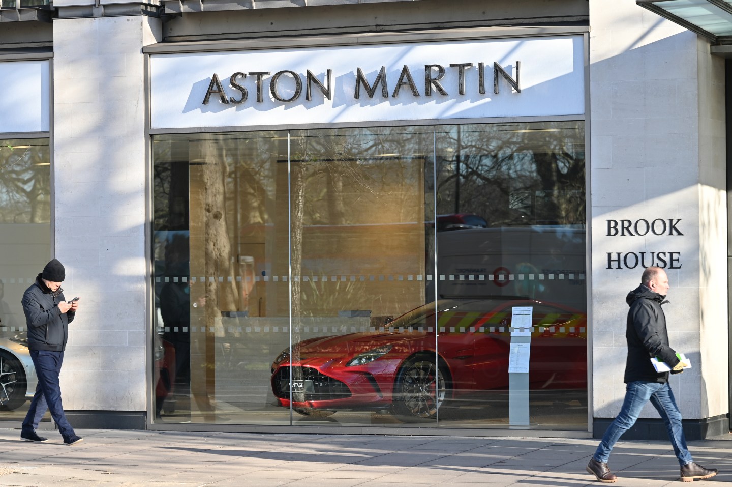 A red Aston Martin Vantage on desplay behind a glass wall with a sign the reads Aston Martin above it.