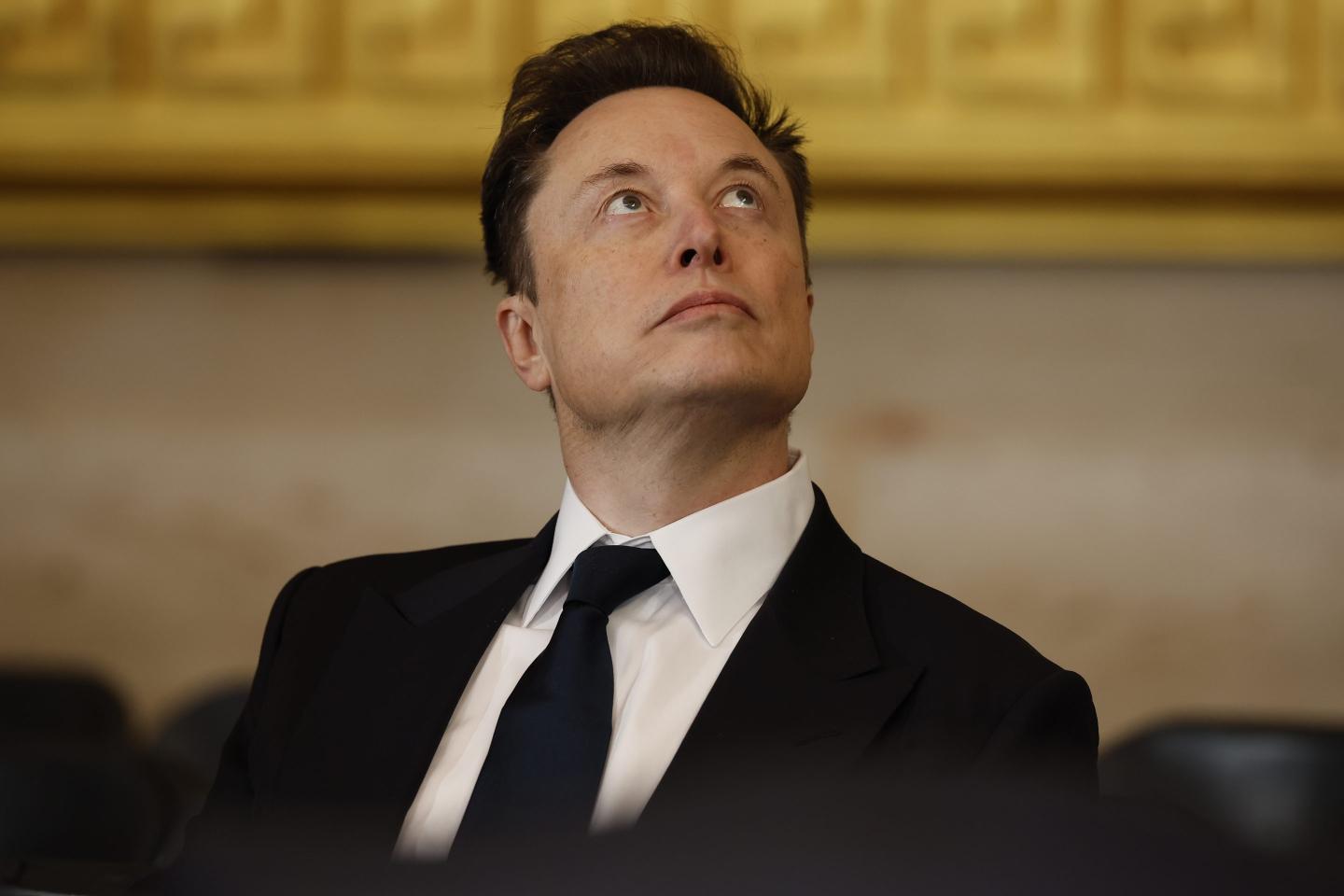 Elon Musk, wearing a suit, stares up at the ceiling