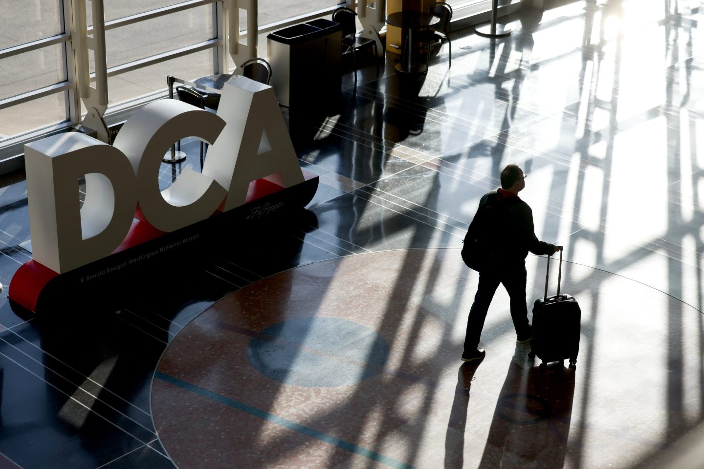 A passenger with a suitcase walks down an airport corridor.