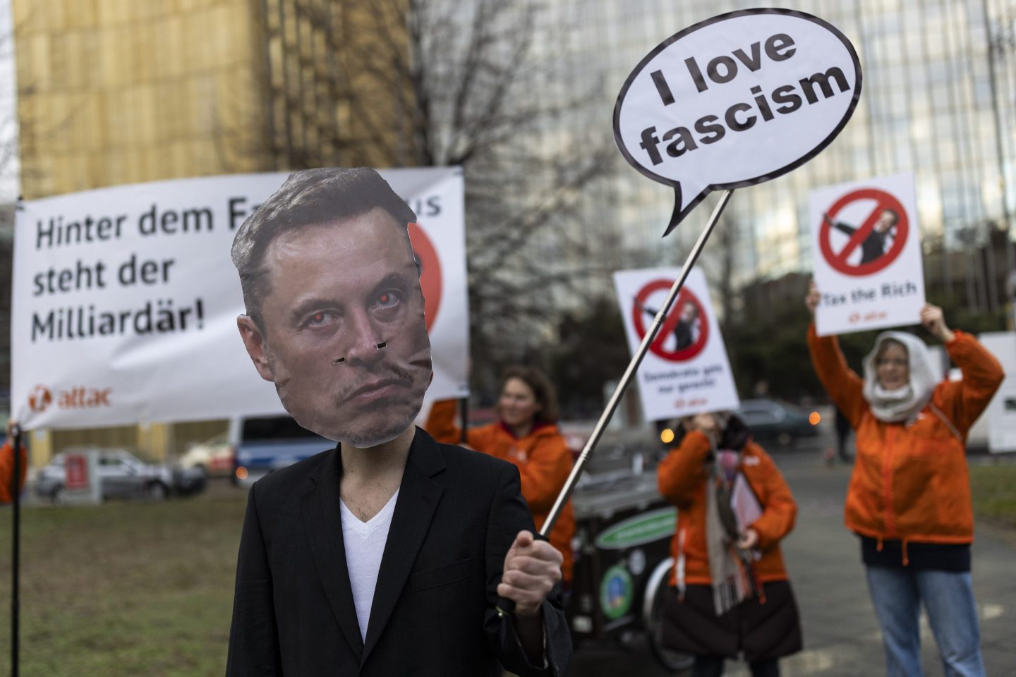 A protester wears an Elon Musk face mask and holds a sign that says, "I love fascism"