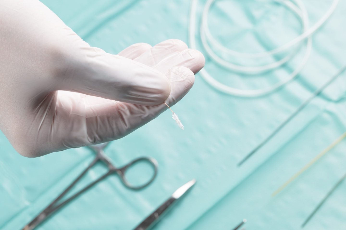 A gloved hand of a surgeon holding Robeauté's microrobot above a draped table with surgical instruments.
