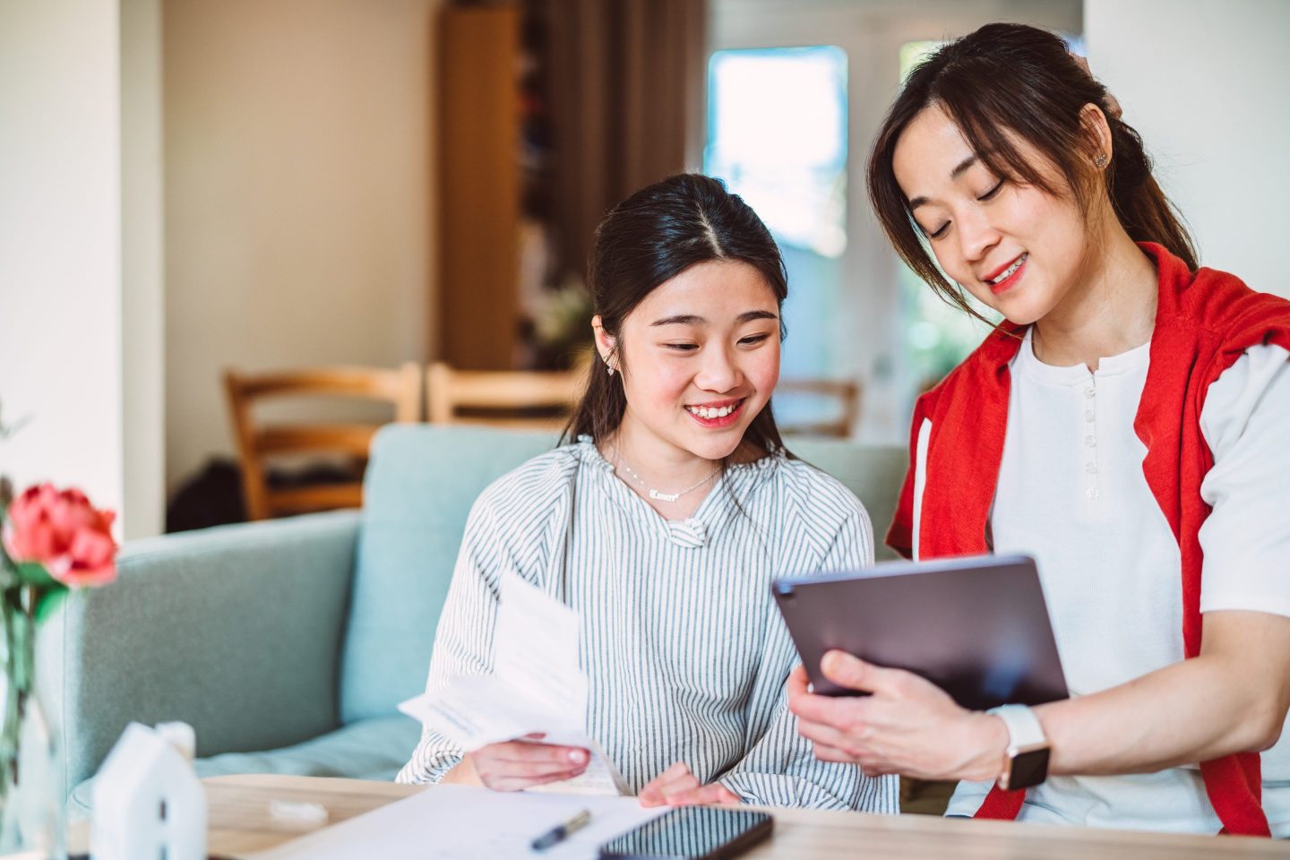 Young mother teaching her teenage daughter finance at home with the aid of AI financial app.