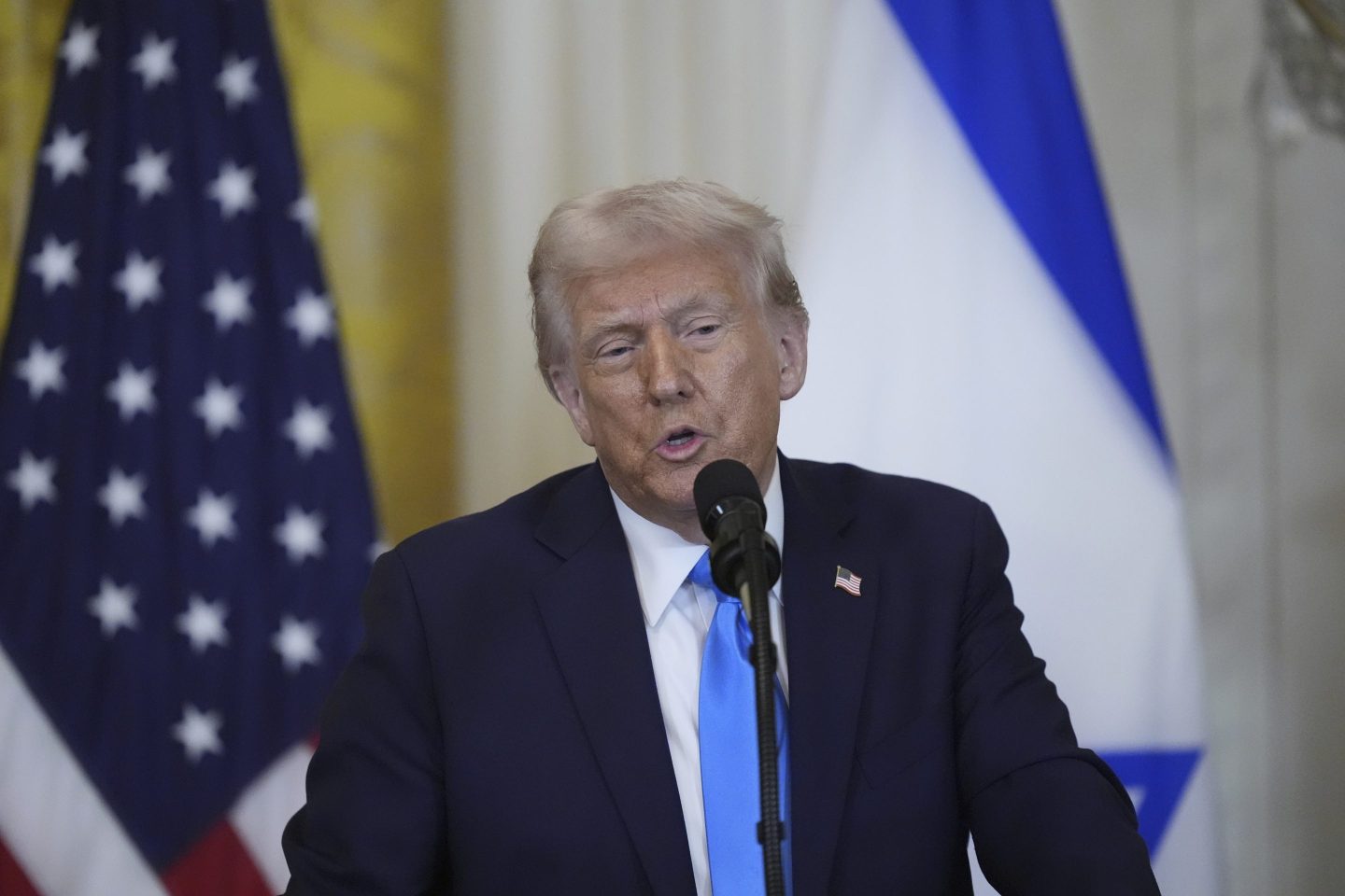 Trump stands in front of two flags and speaks
