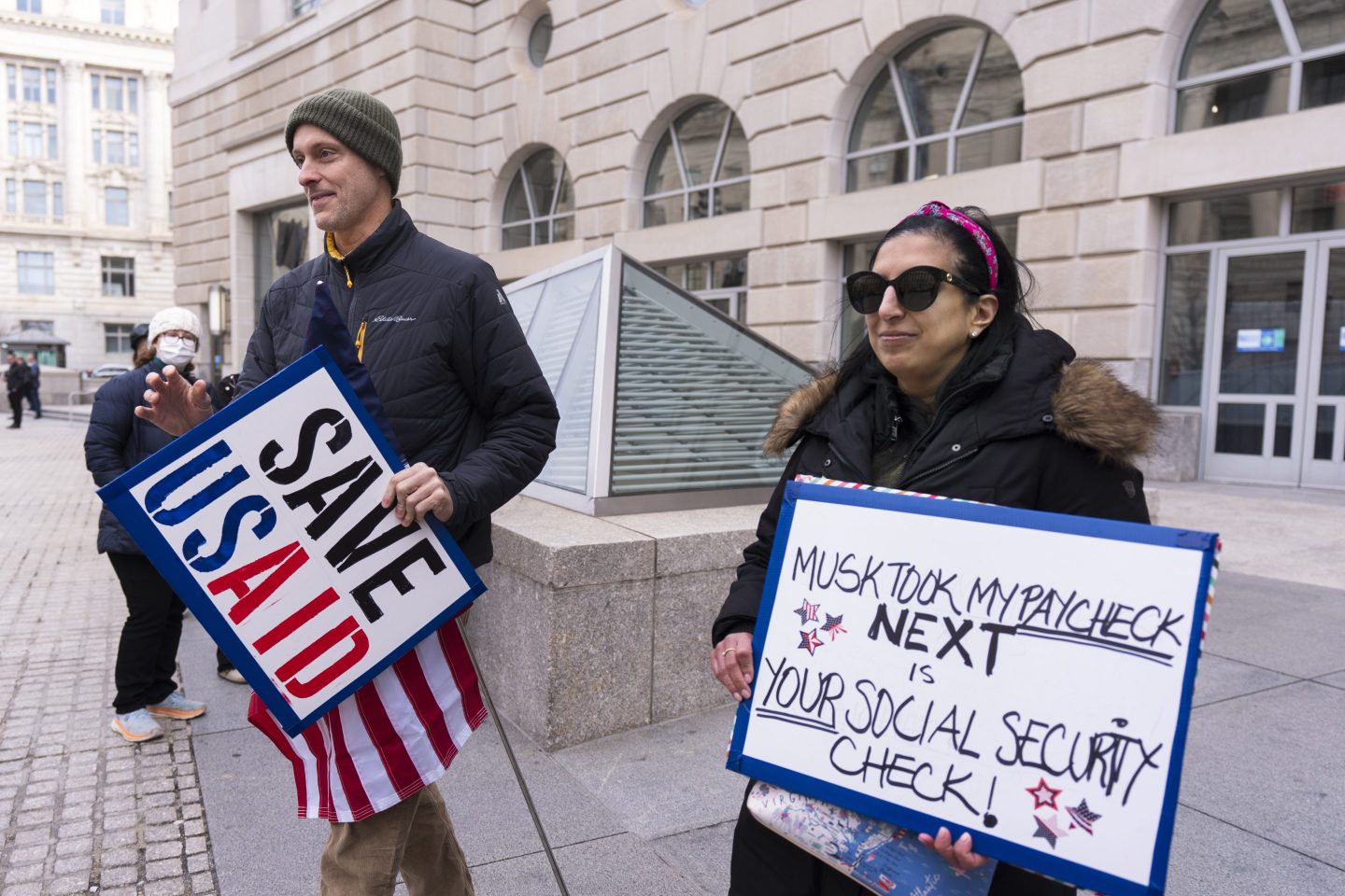 Priya Kathpal, right, and Taylor Williamson, who work for a company doing contract work for the United States Agency for International Development, or USAID, carry signs outside the USAID headquarters in Washington, on Feb. 10, 2025.