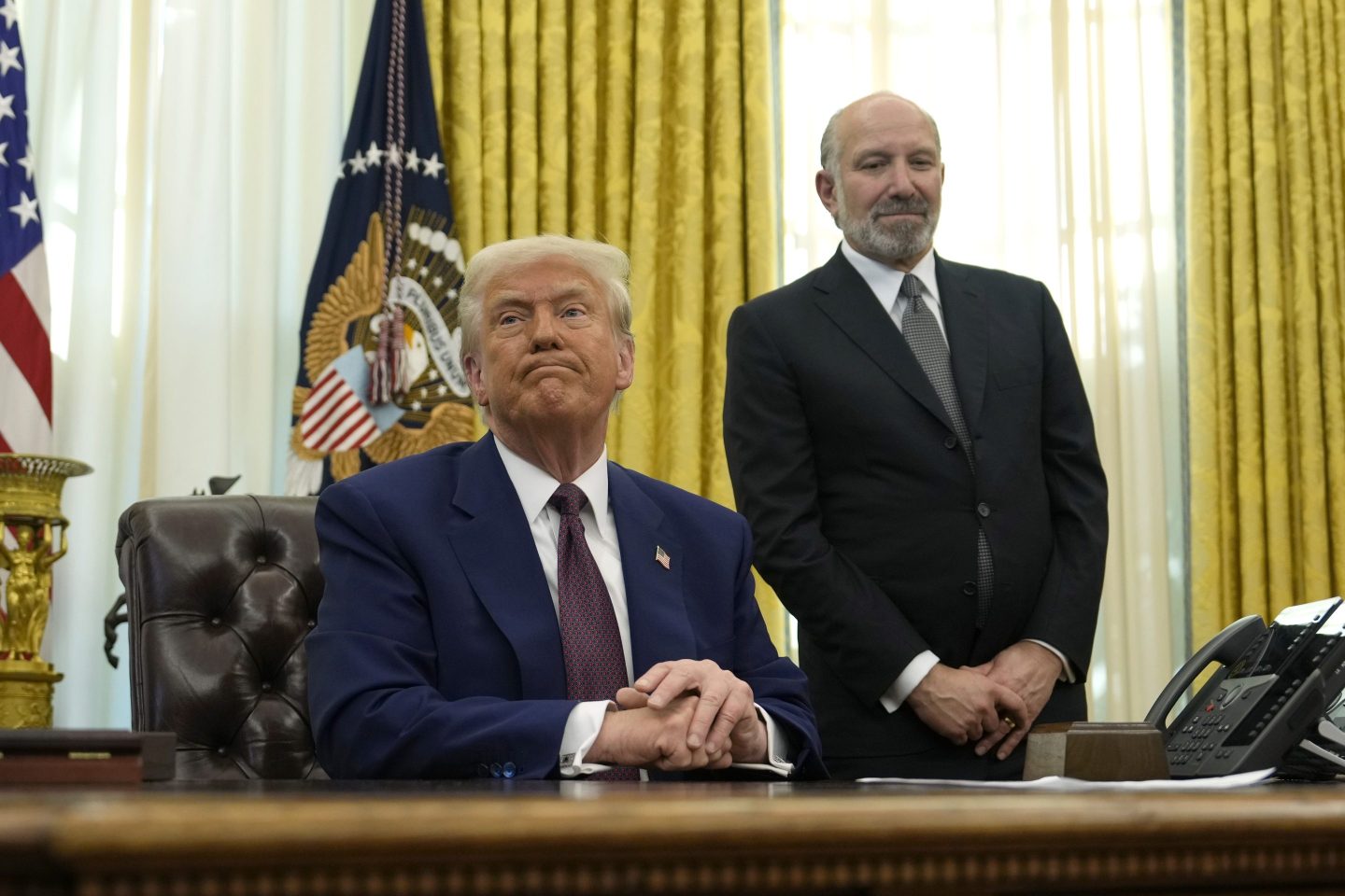 President Donald Trump listens to a question from a reporter as Commerce Secretary nominee Howard Lutnick watches after Trump signed an executive order in the Oval Office of the White House, on Feb. 13, 2025, in Washington.