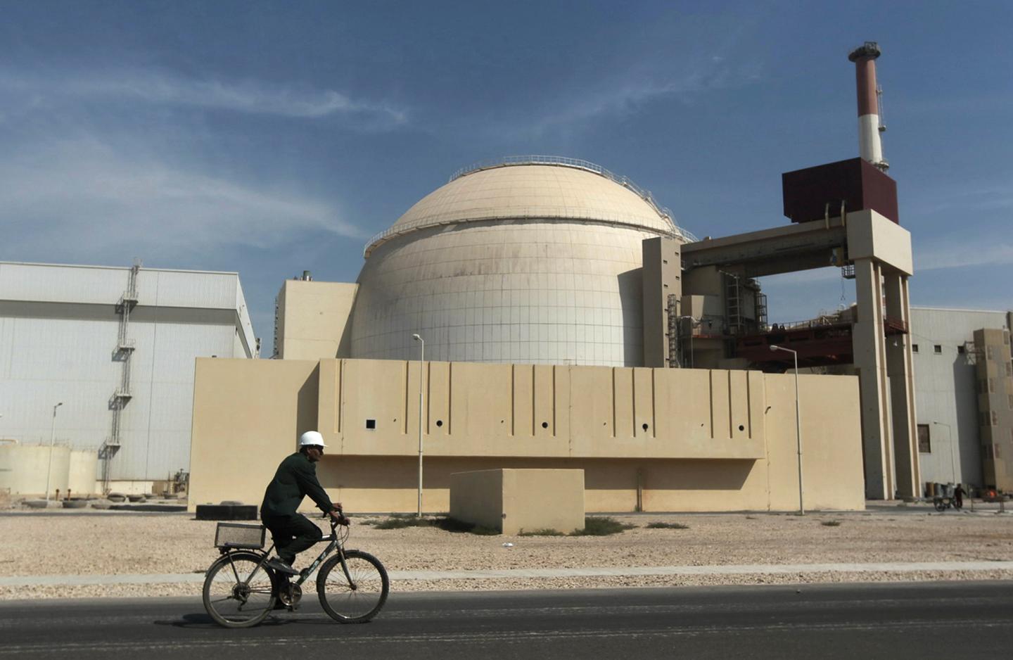 A man rides a bike in front of an Iranian nuclear reactor building