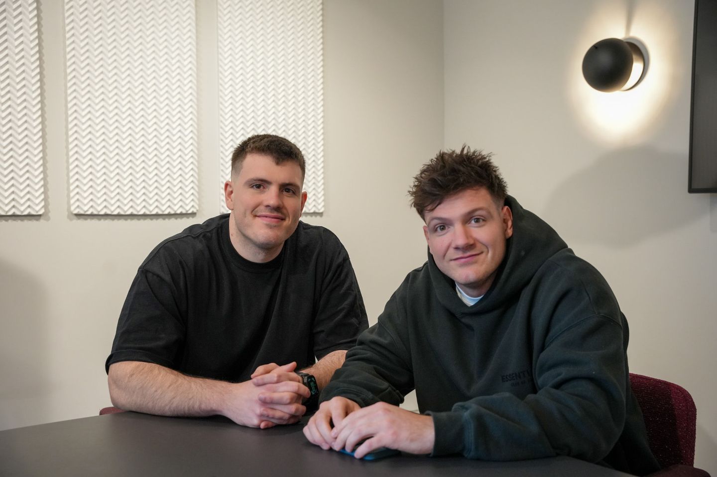 two men in casual clothing sit at a table, posed for a photo portrait