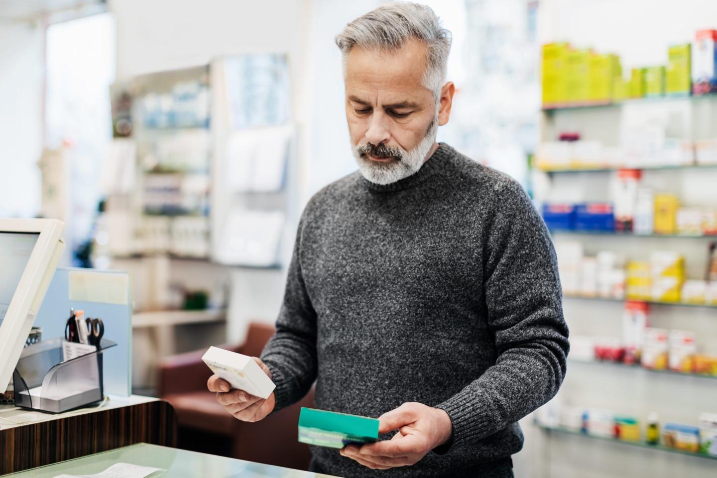A middle-aged man picks up his medications at a pharmacy.