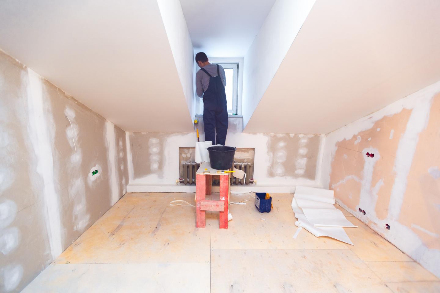 Worker is installing pvc window from wooden platform in small room of apartment that is under construction