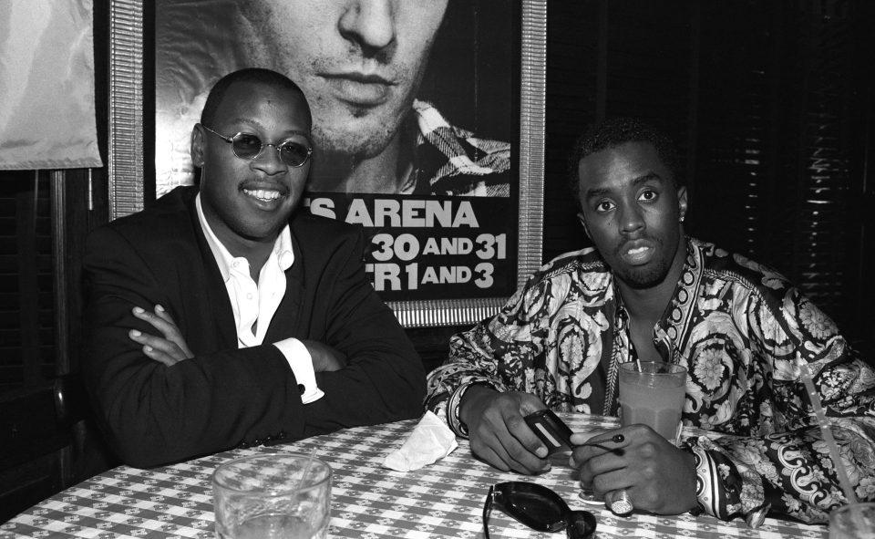Andre Harrell and Sean Combs sitting at a table with a gingham tablecloth, looking at the camera.