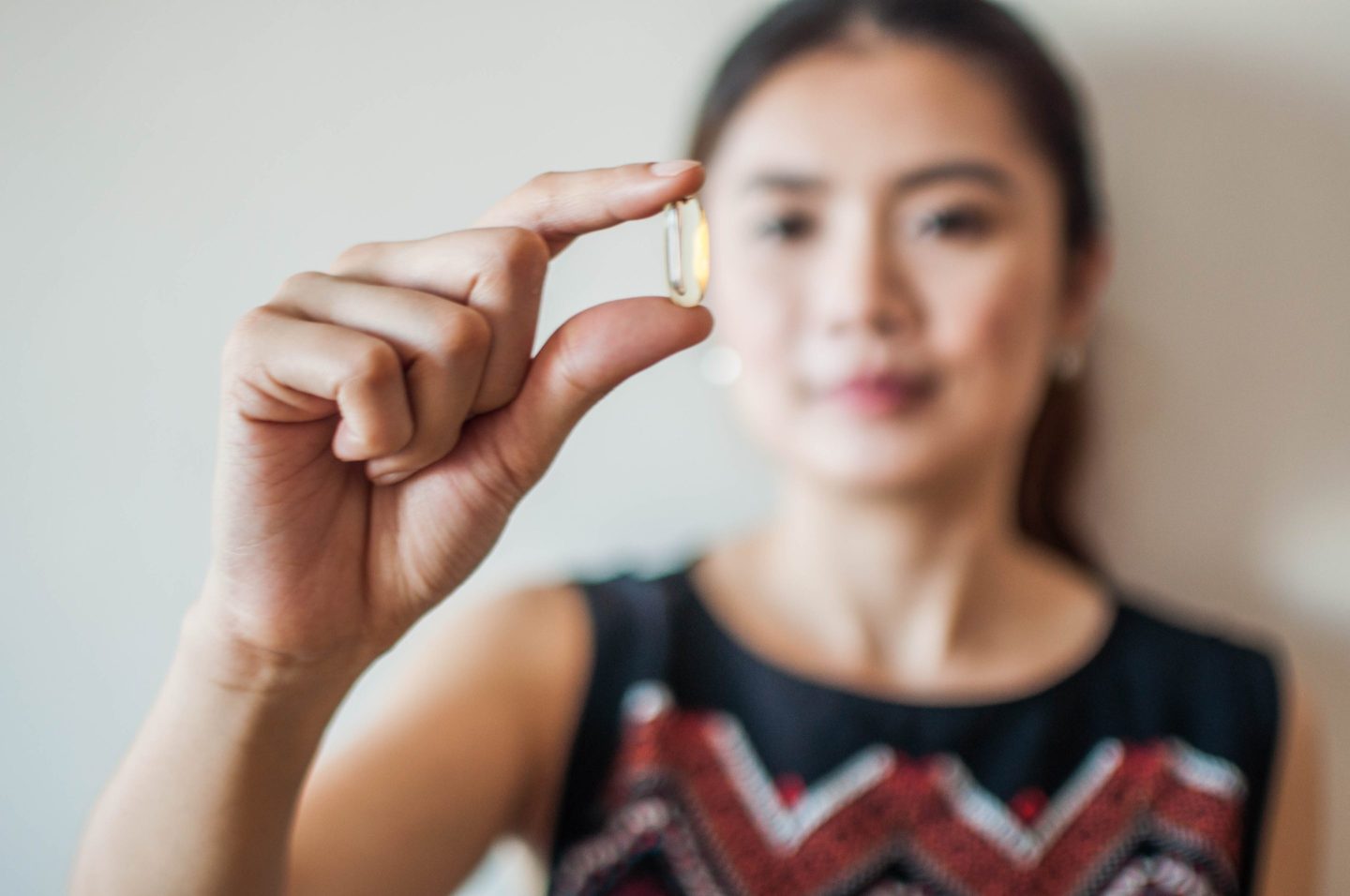 Woman in background holding gel cap vitamin in foreground