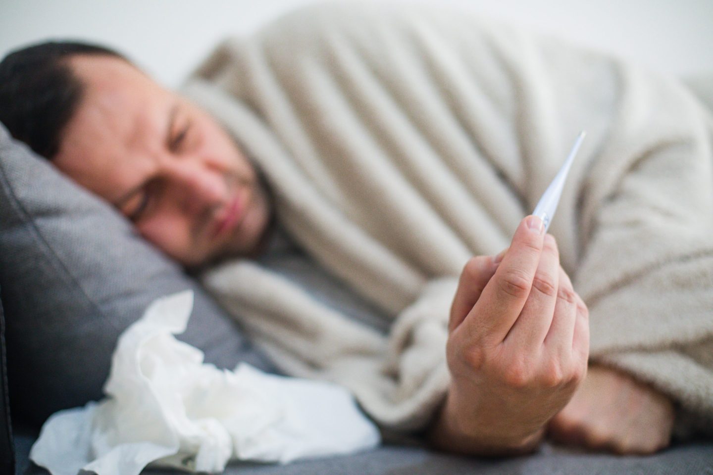 Sick man in bed checking fever with thermometer