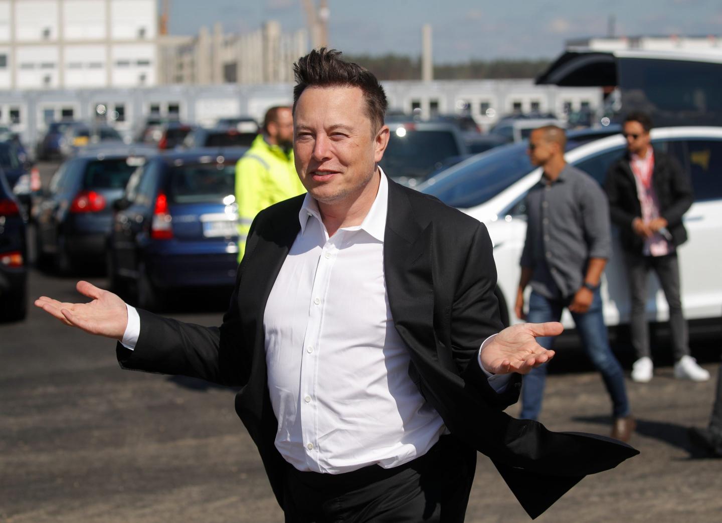 Elon Musk gestures in front of a group of cars