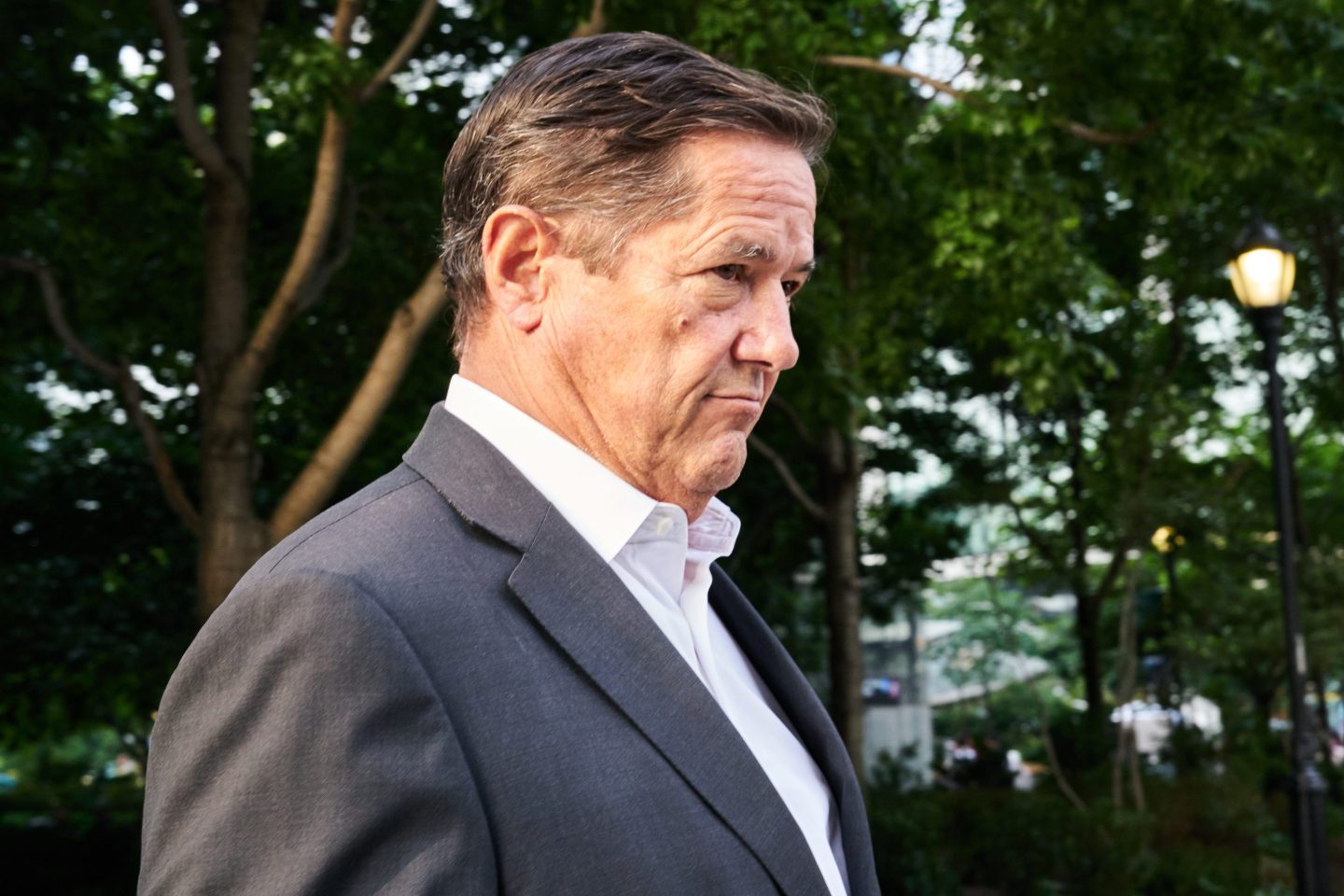 Jes Staley, stoic, stands in front of a thicket of trees.