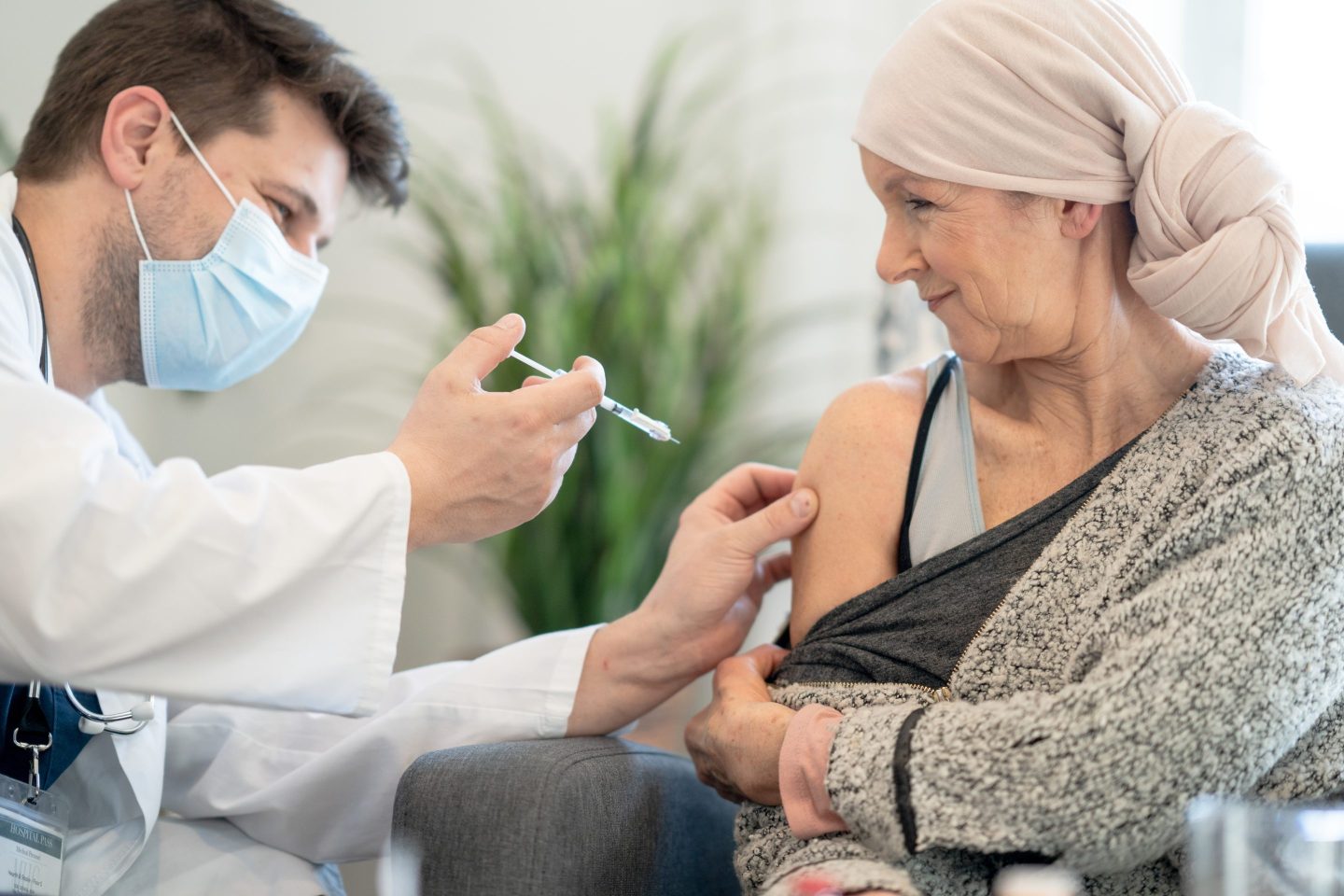 A woman wearing a head wrap gets a vaccine from a masked doctor