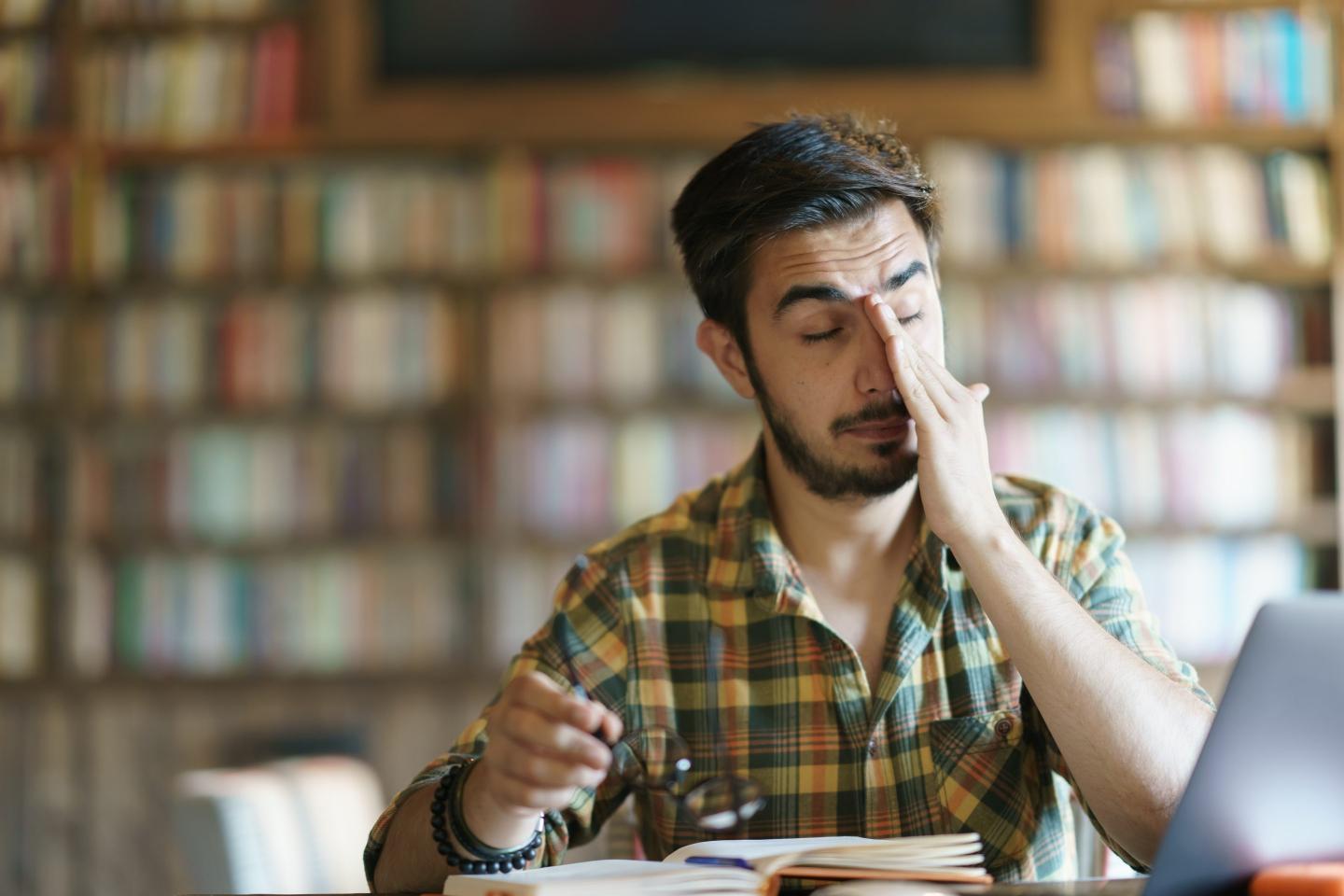 A person in a library rubbing their face.