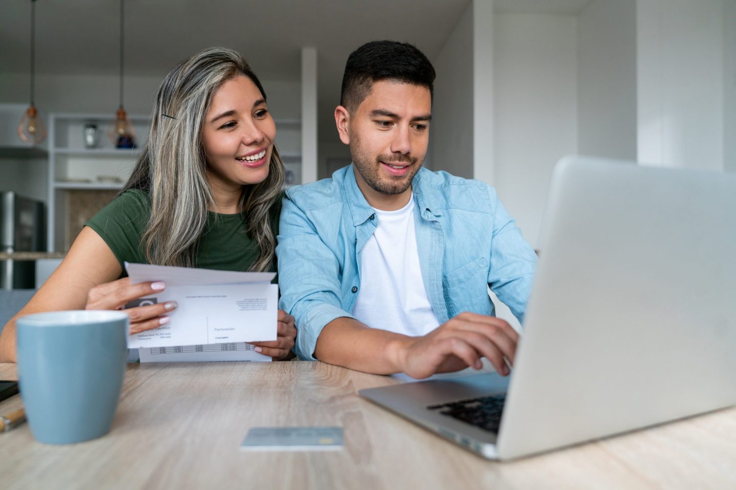 A smiling couple looks at a laptop as they pay their bills