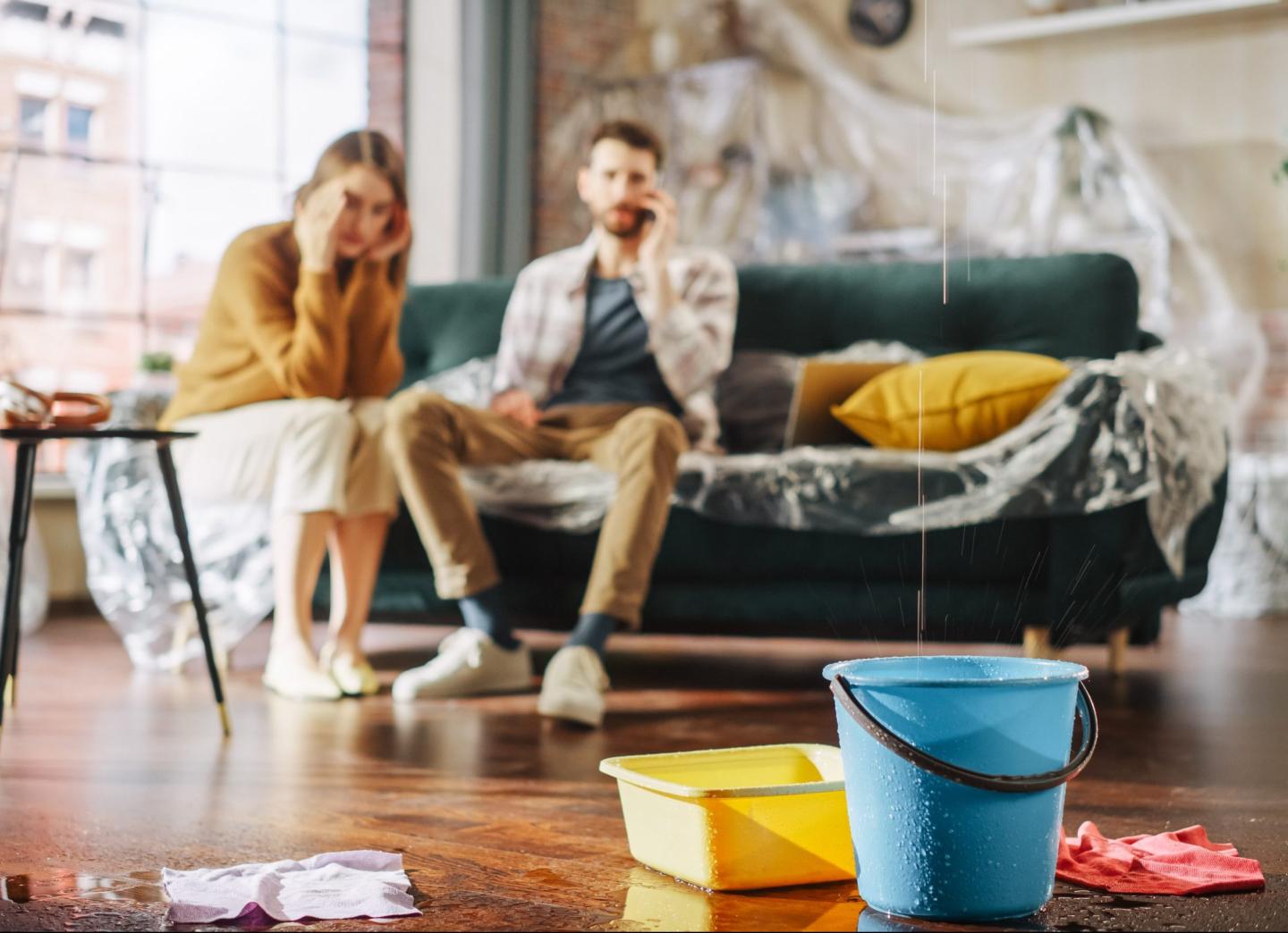 Two people sitting in a room dealing while a leak is dripping into a bucket.