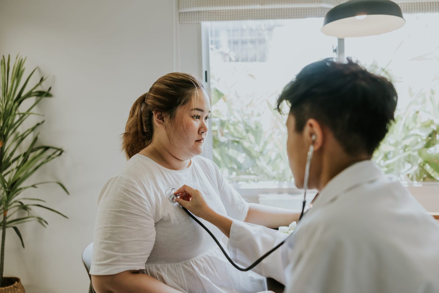 Doctor listening with a stethoscope to the heart of an overweight Asian woman