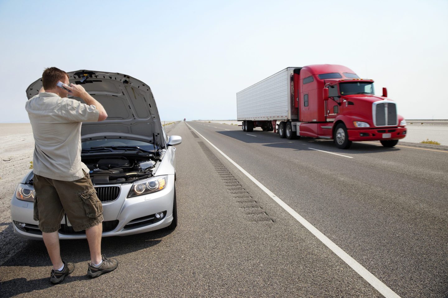 A person looking in the hood of their car on the side of the road.