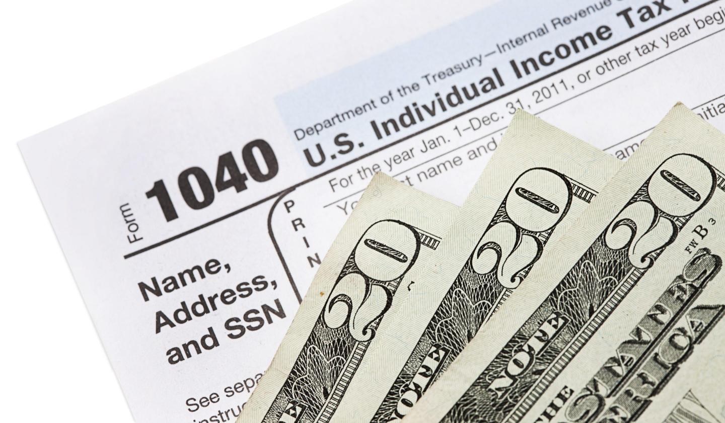 Twenty dollar bills next to an IRS 1040 form.