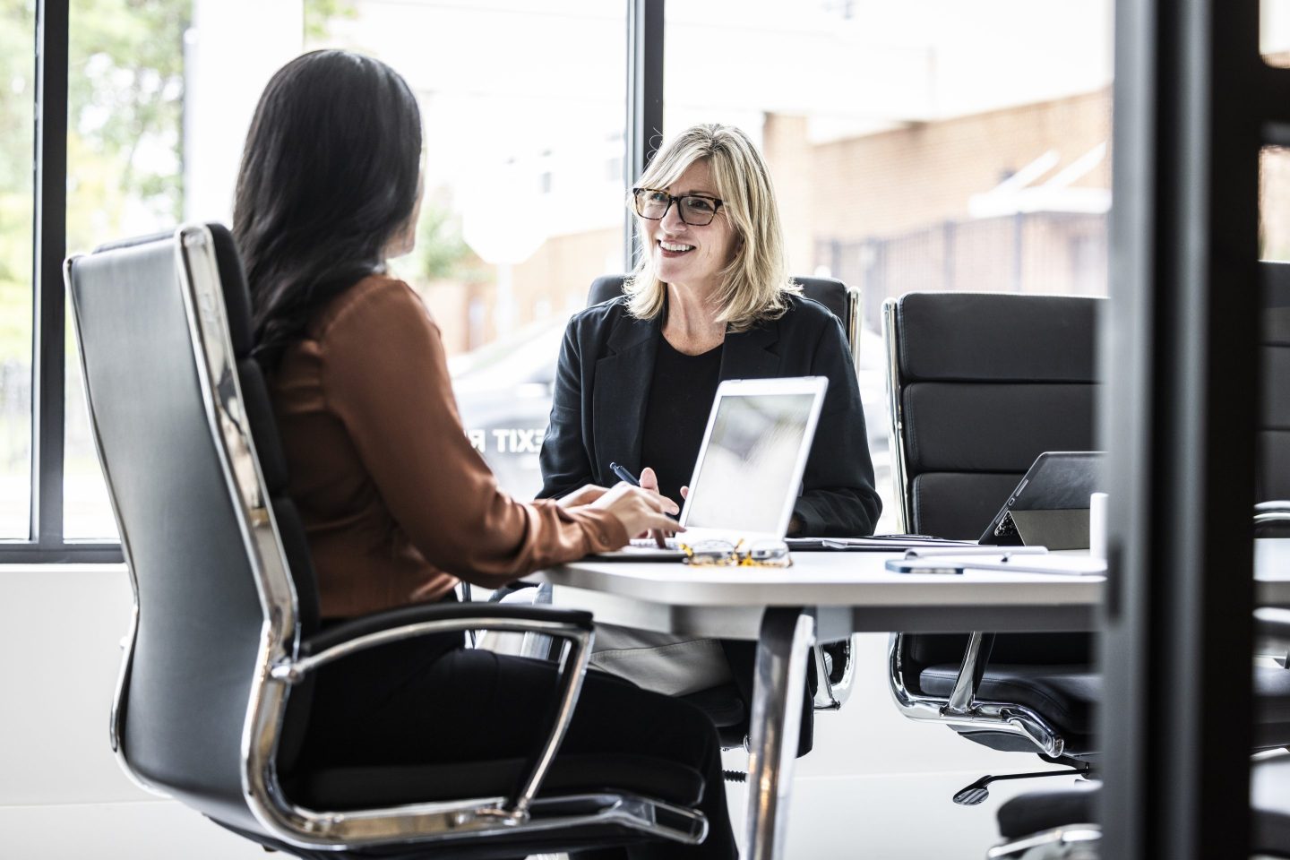 A woman sits in a job interview, at a desk, across from another woman doing the hiring