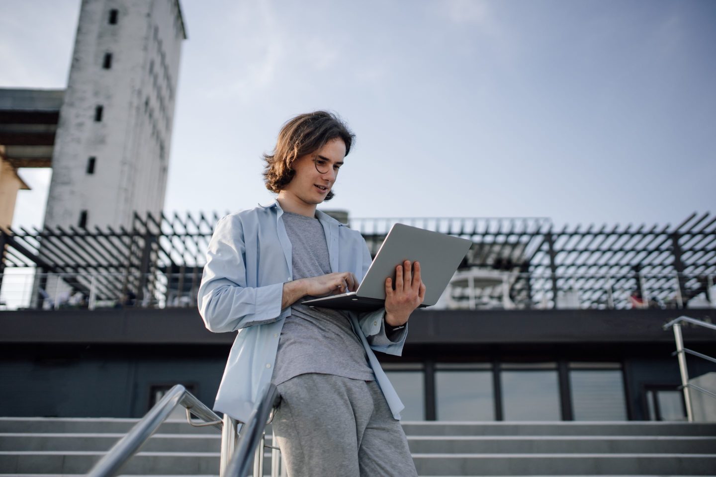 Young man holding laptop outside and typing