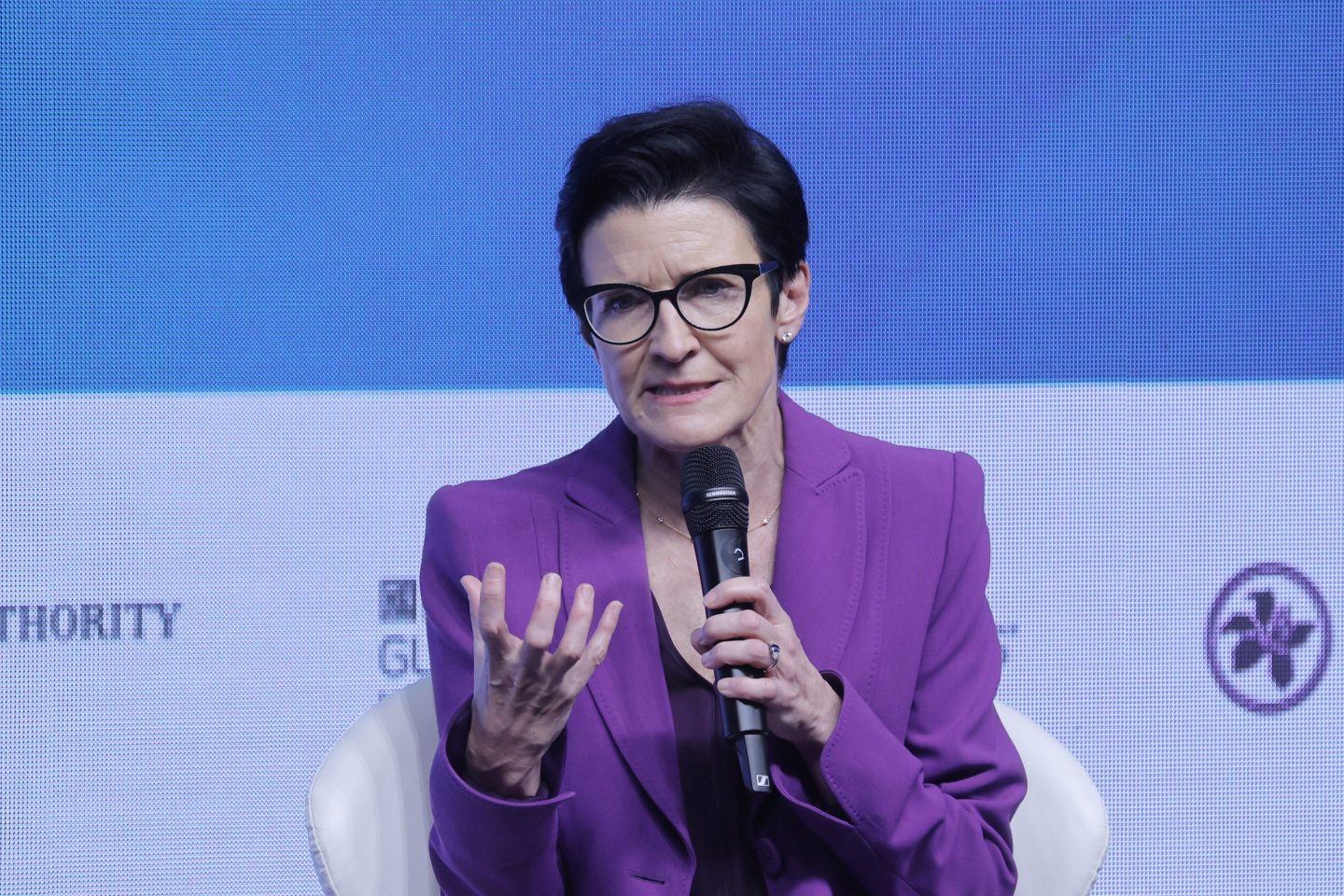 Jane Fraser speaks into a microphone and holds up her hand