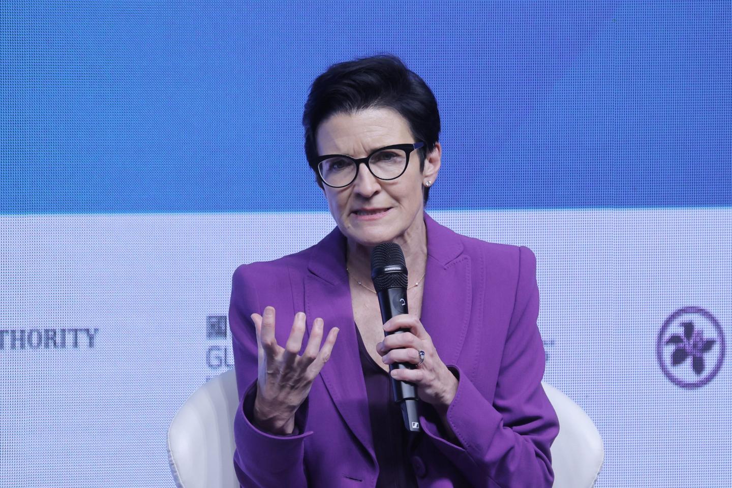 Jane Fraser speaks into a microphone and holds up her hand