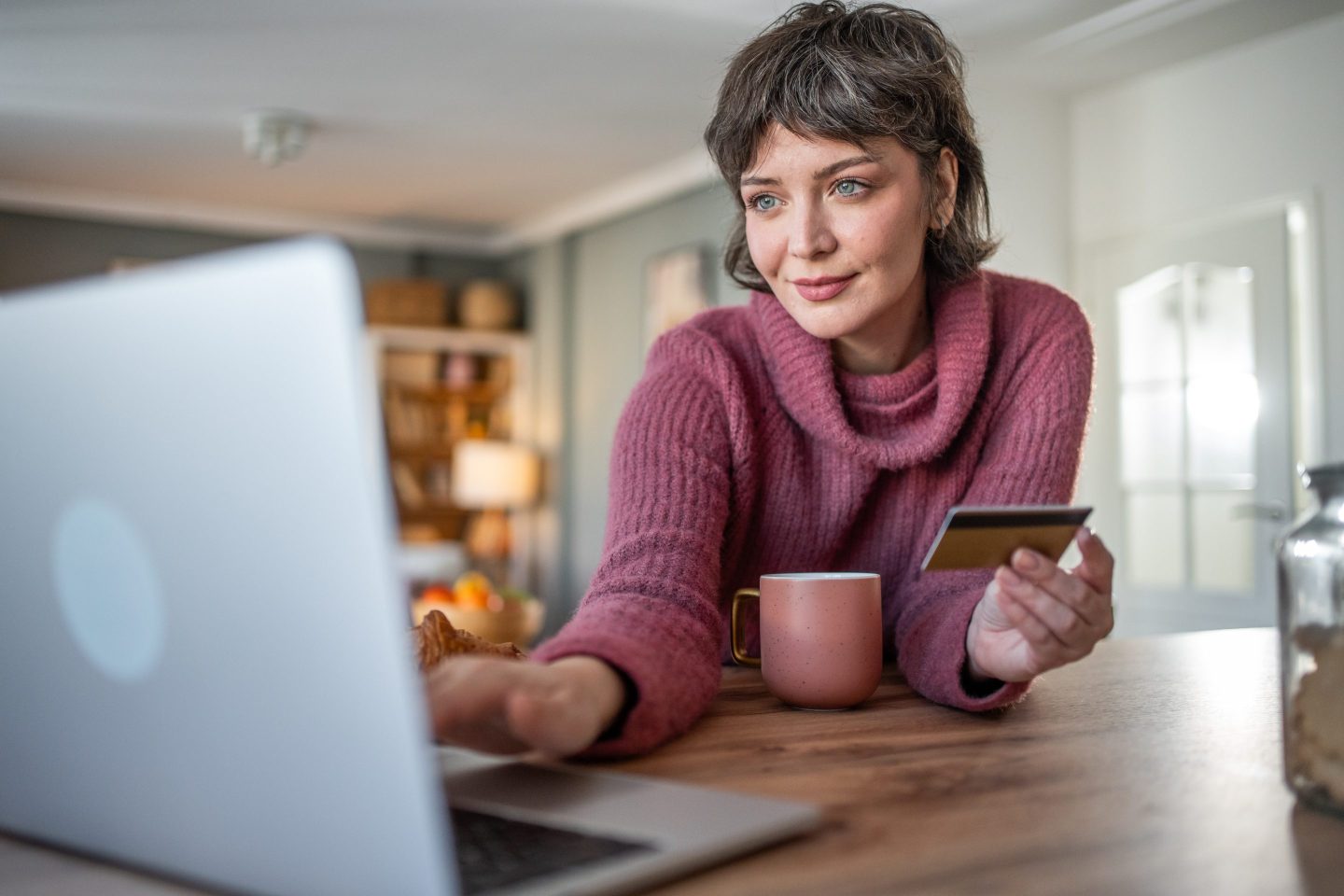 A person sits with a cup of coffee holding a credit card.