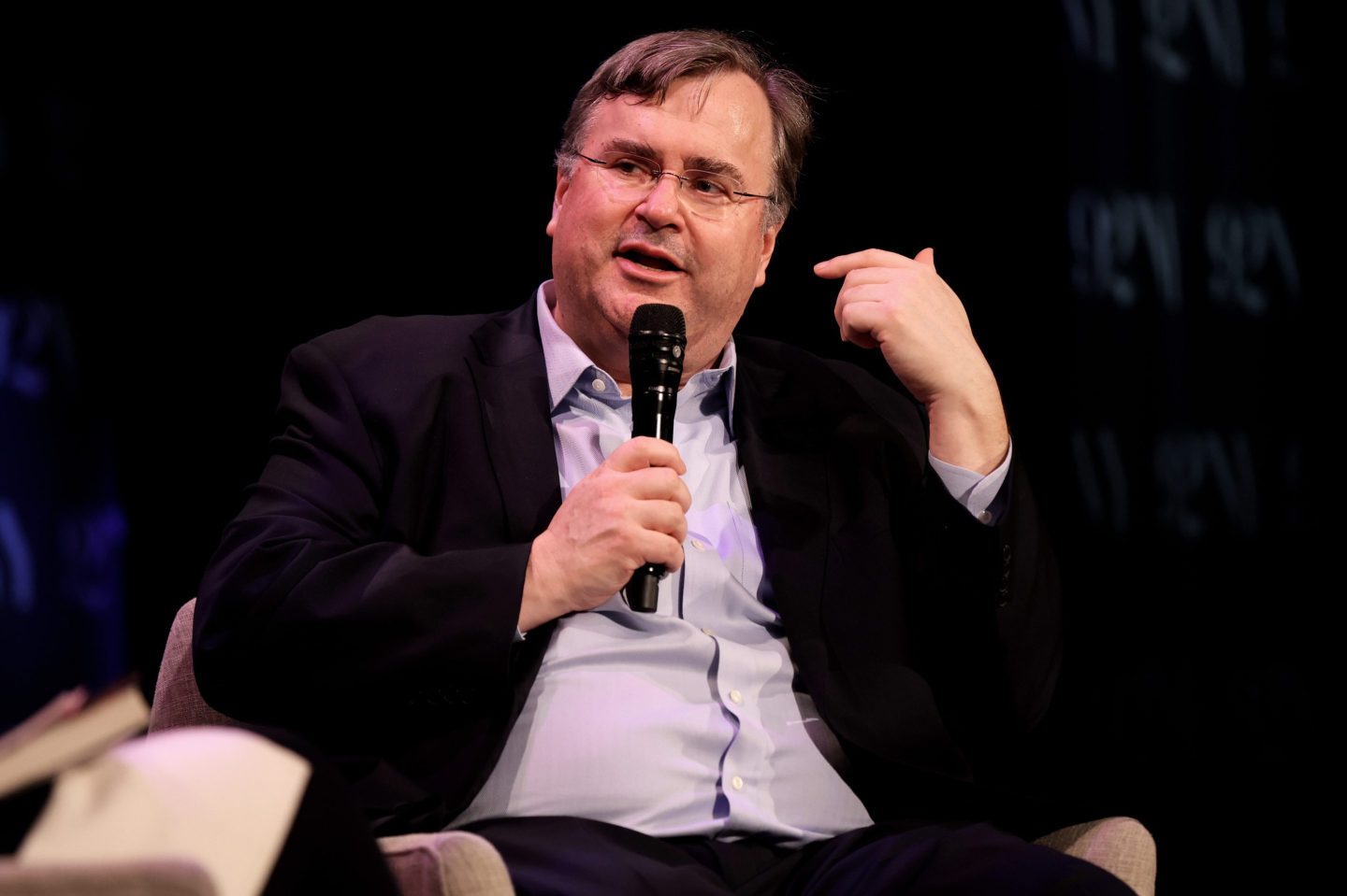 LinkedIN Cofounder and venture capitalist Reid Hoffman sitting on staqe holding a microphone.