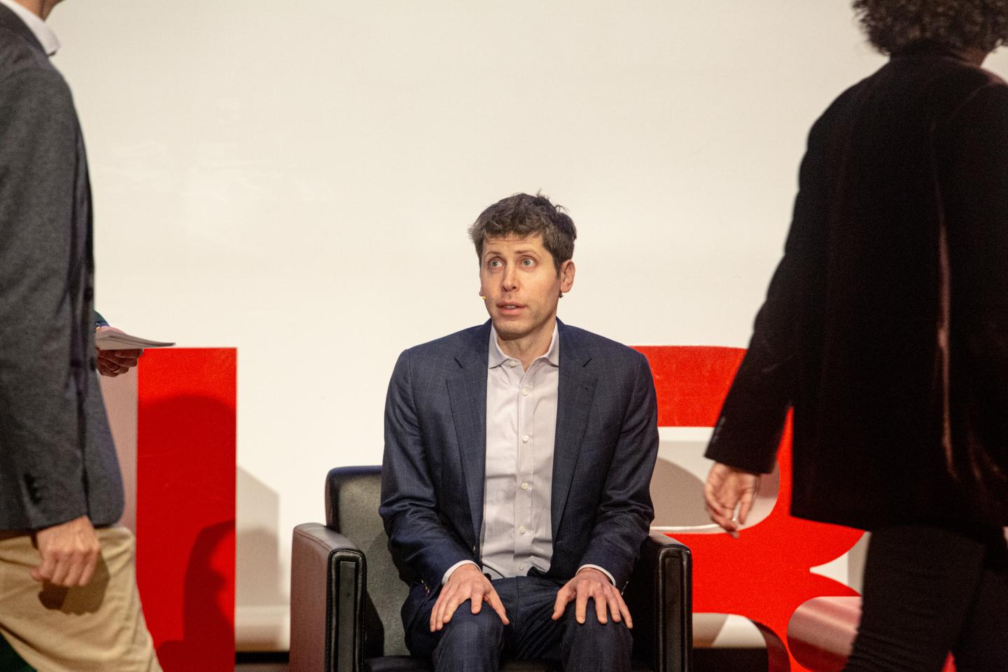Sam Altman in a suit sitting on a stage.