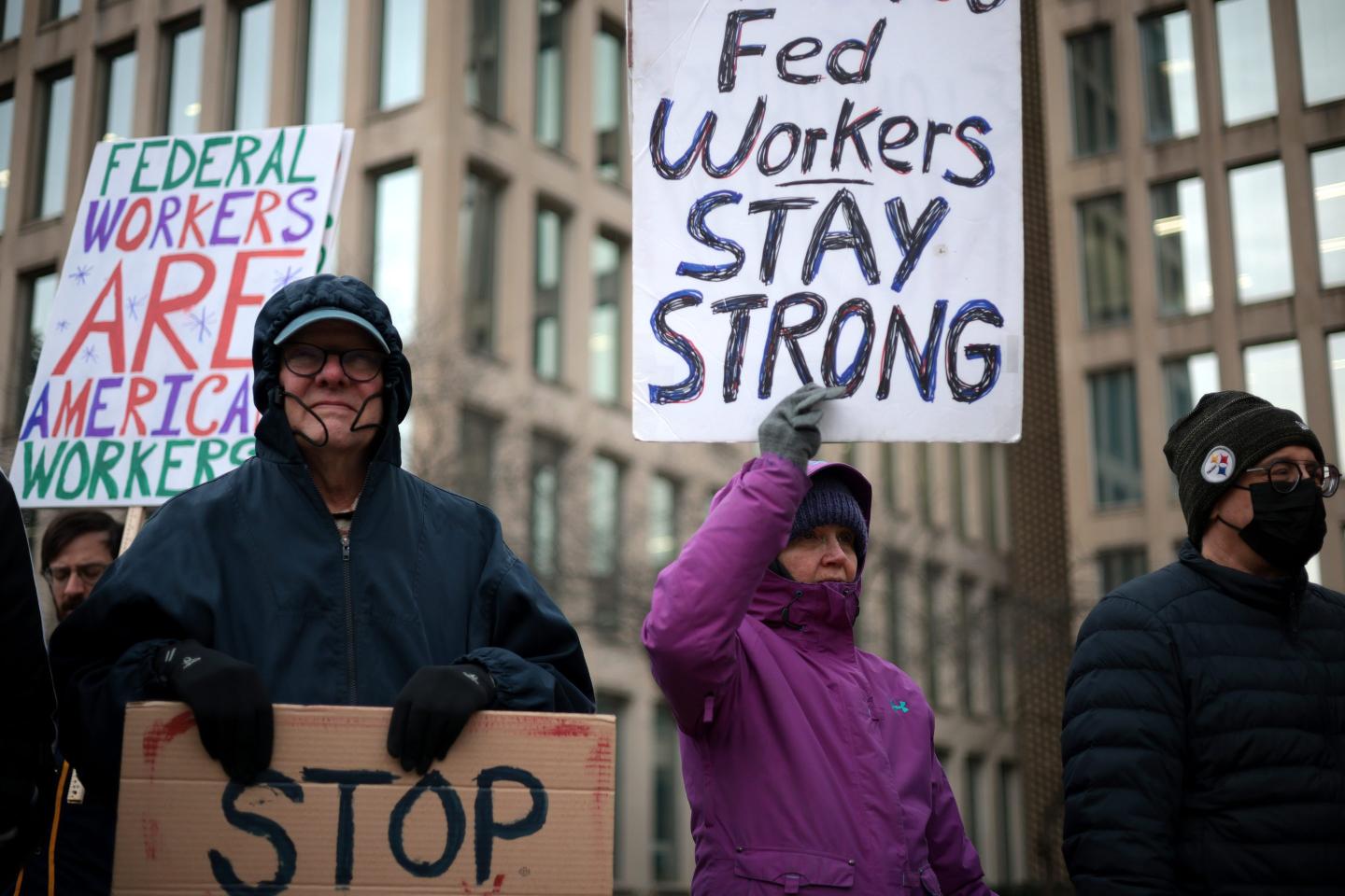 adults stand outdoors holding protest signs
