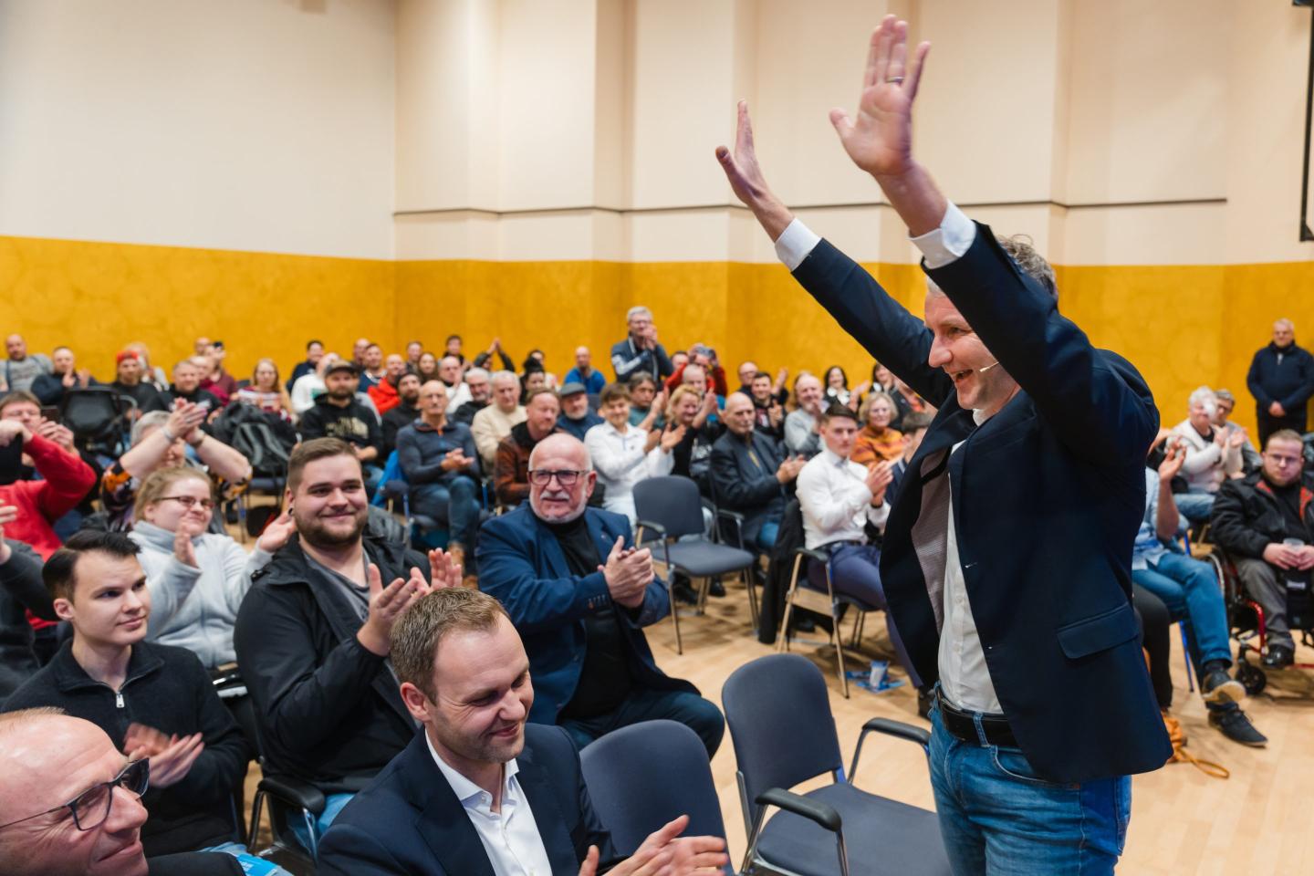 A man raises his hands in a room full of people