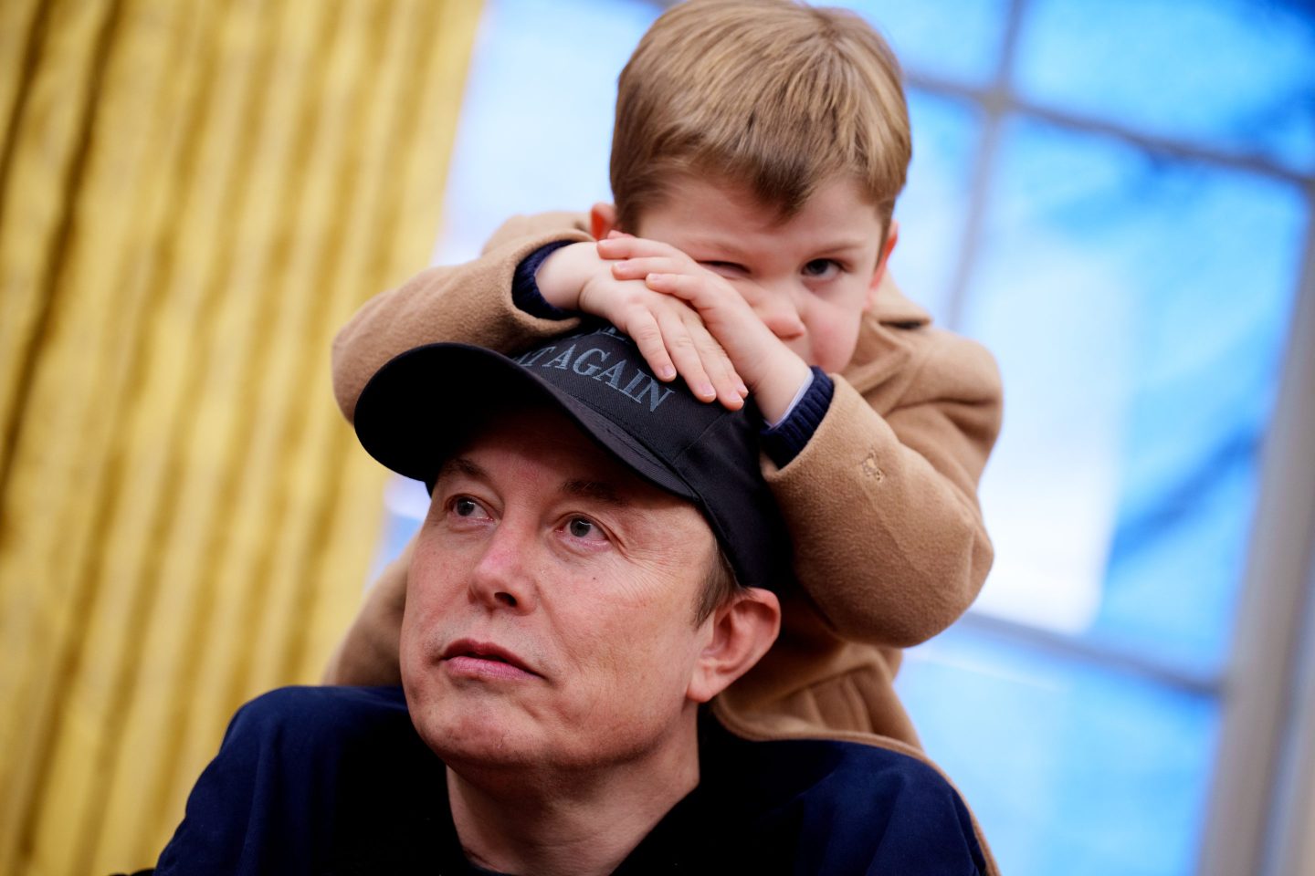 Elon Musk's son, X Æ A-Xii, sits on his father's shoulders during a press conference in the Oval Office.