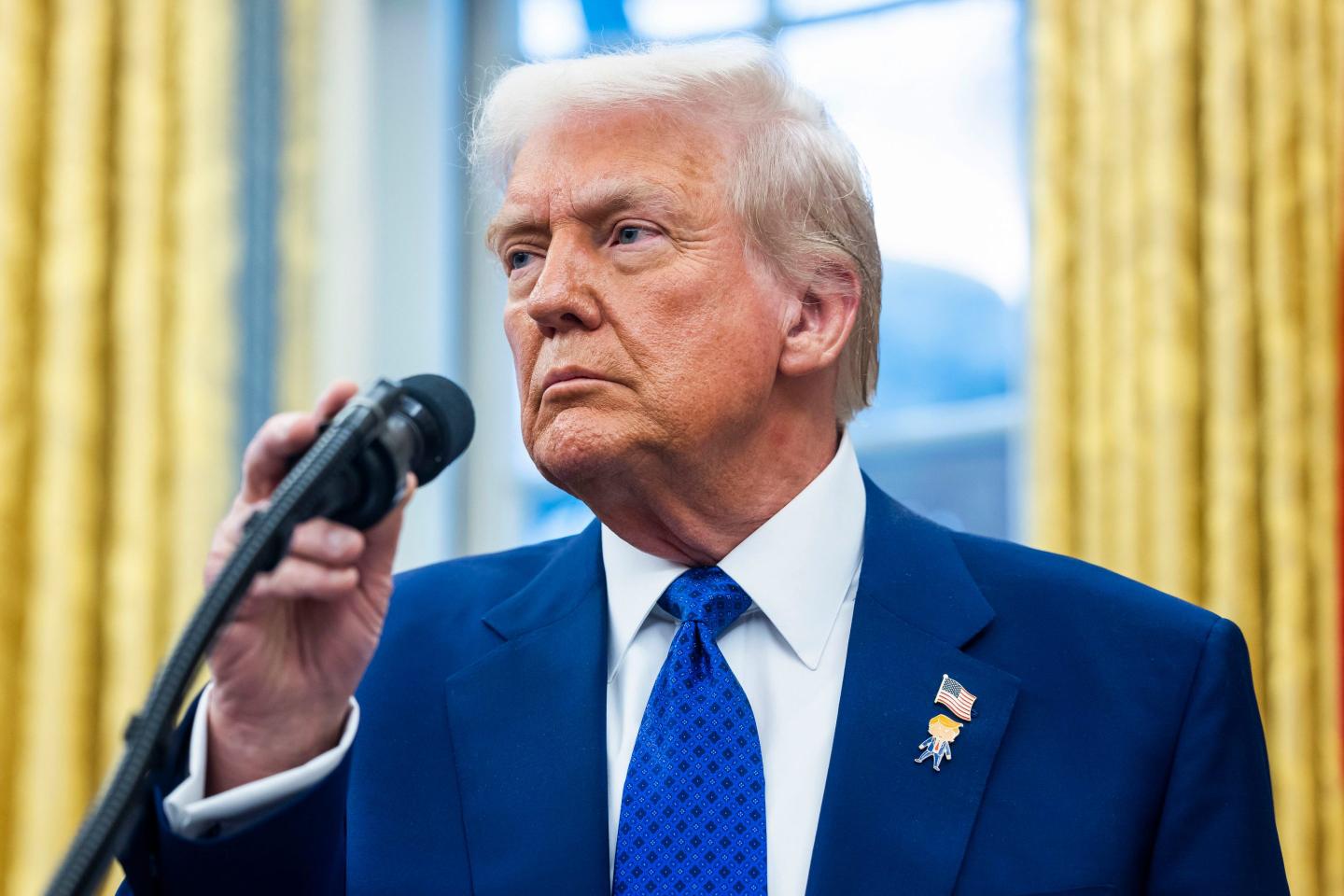 Donald Trump looks to the left and holds a microphone in his hand