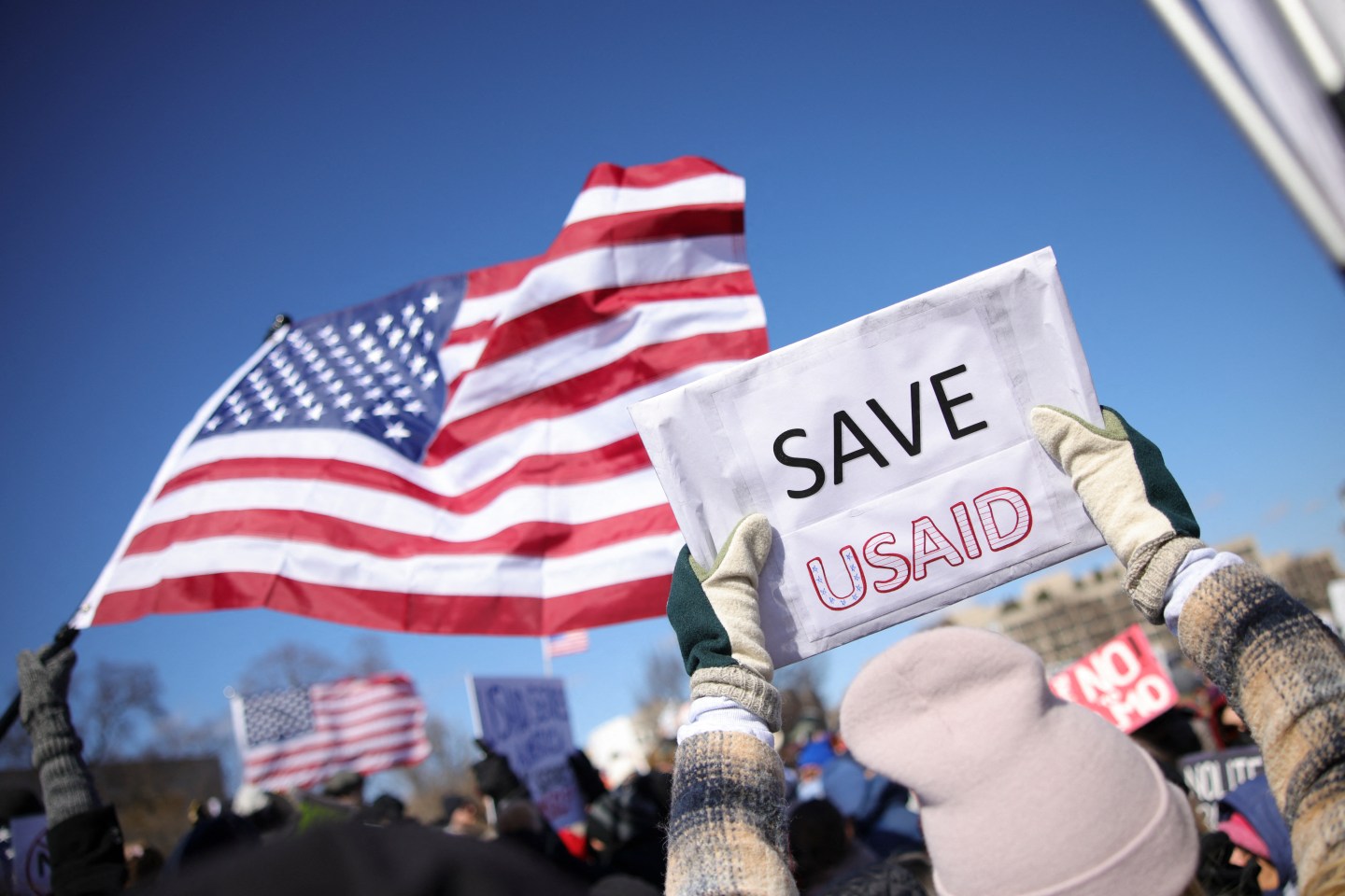 Picture of the US flag behind a sign saying "Save USAID."