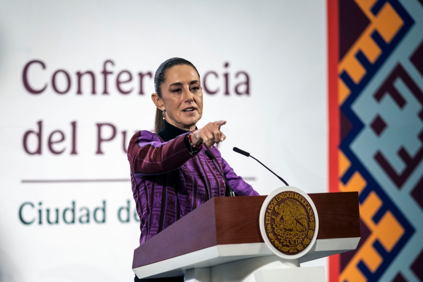 Mexico President Claudia Sheinbaum stands in front of a podium and points into the crowd